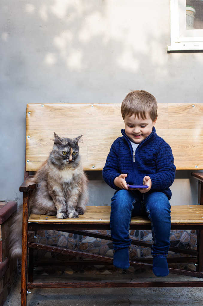 Little boy looking at a mobile phone with a cat by Oleksandra Mykhailutsa on 500px.com