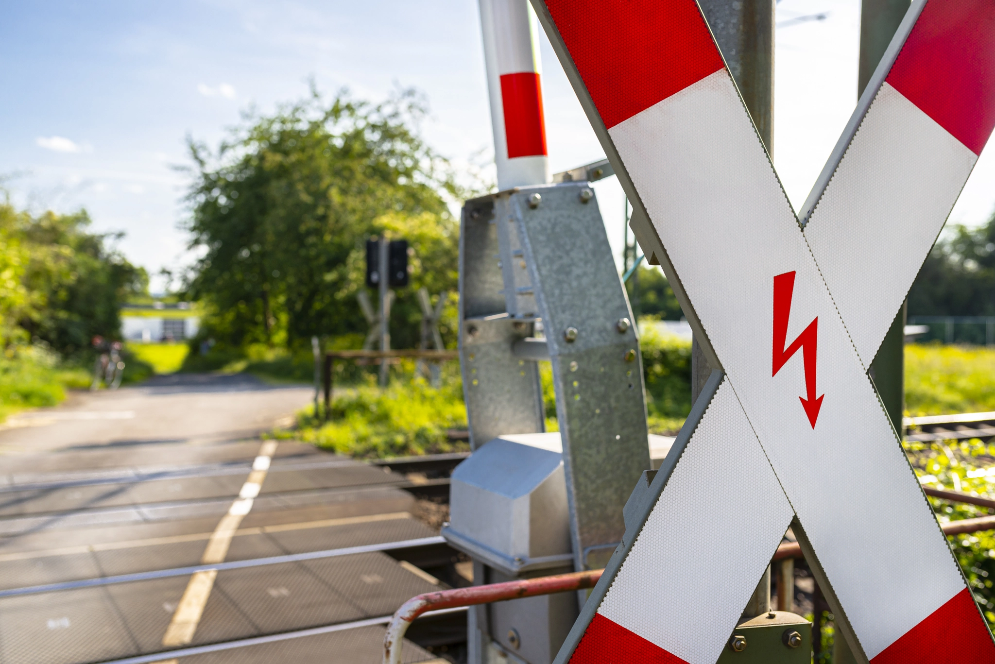 Guarded railroad crossing in the countryside with open barriers.