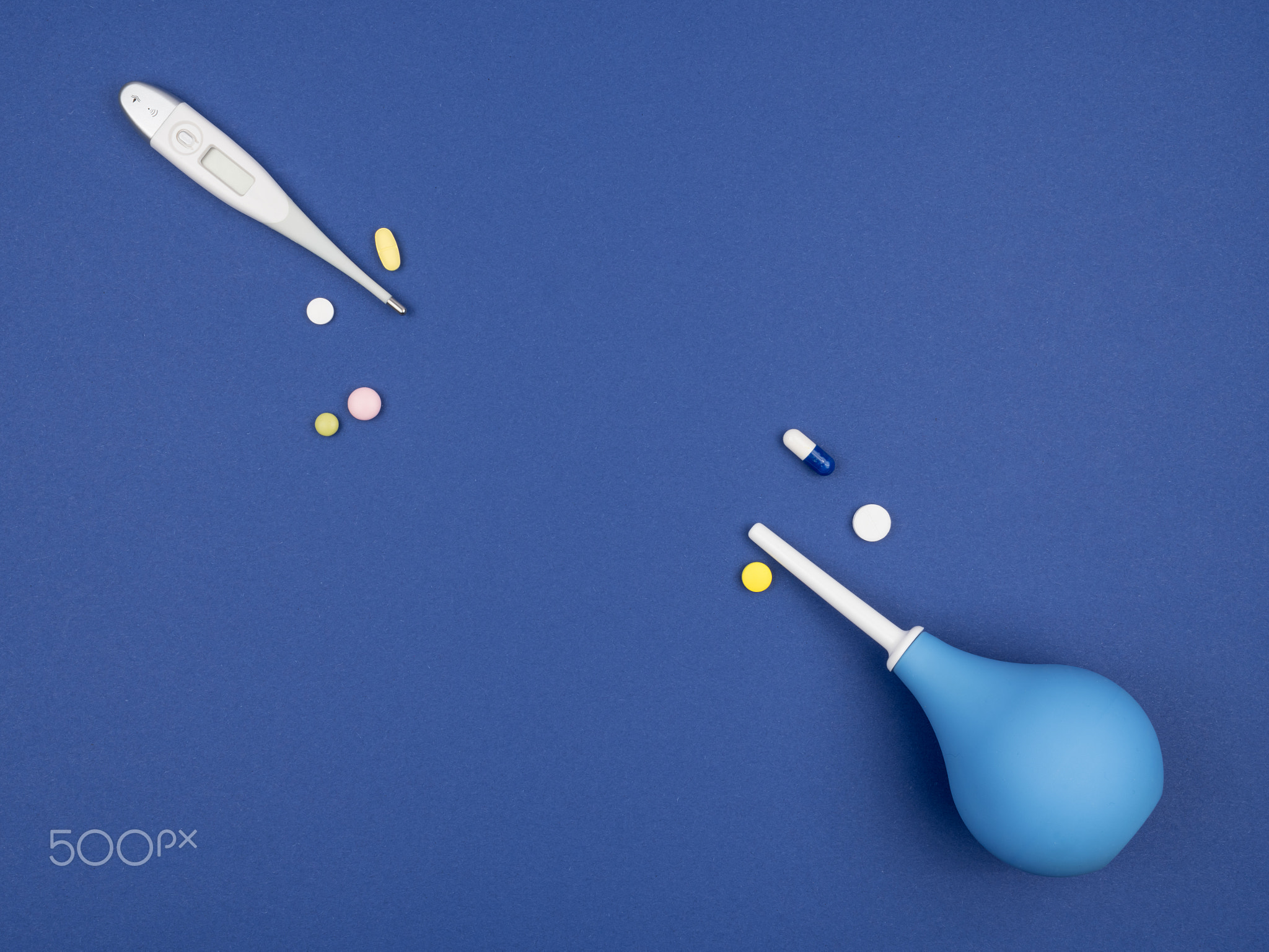 Enema pear, a thermometer and pills on a blue background.