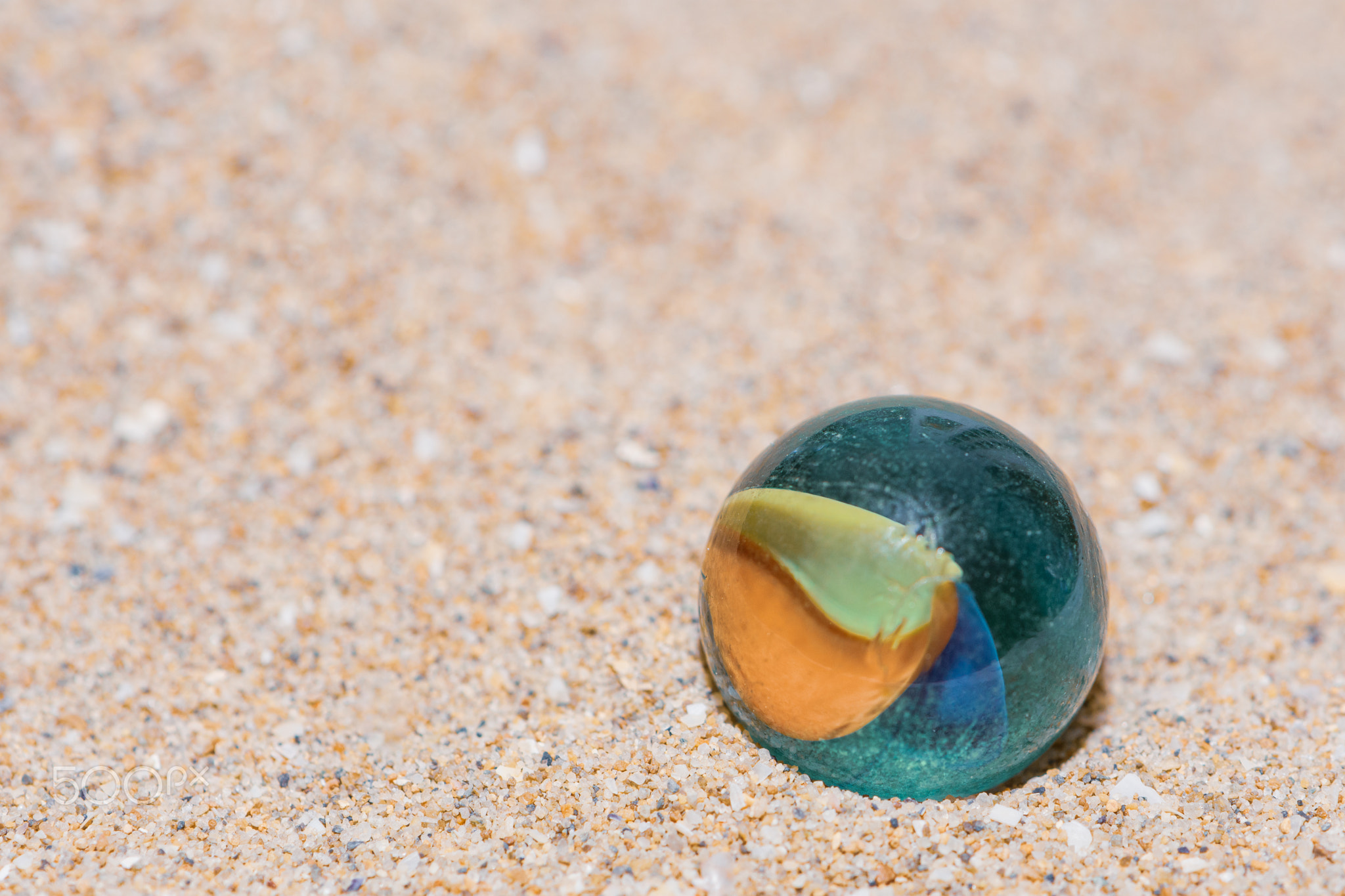 Glass marble with colored interior resting on the sand