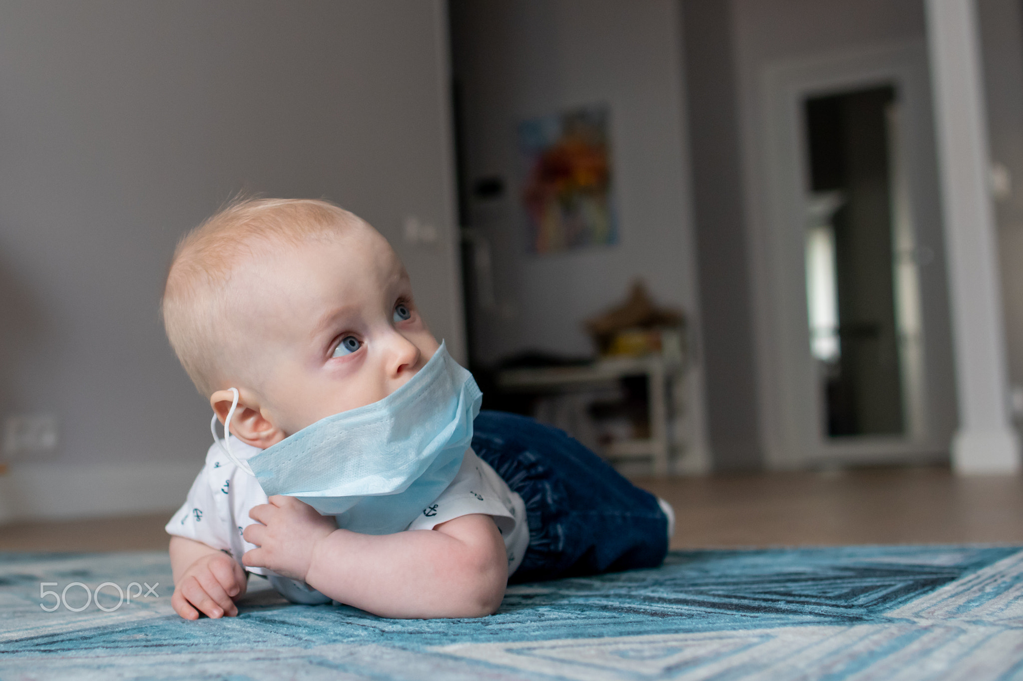 White caucasian baby boy in a face mask lying on the blue geometric