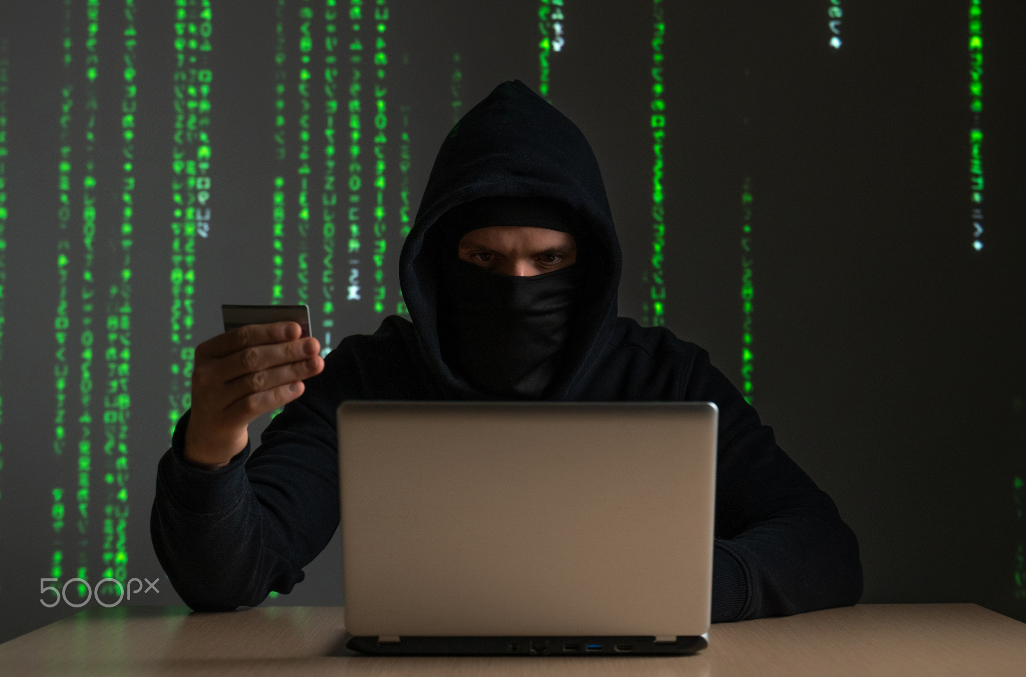 Computer hacker with credit card stealing data from a laptop concept