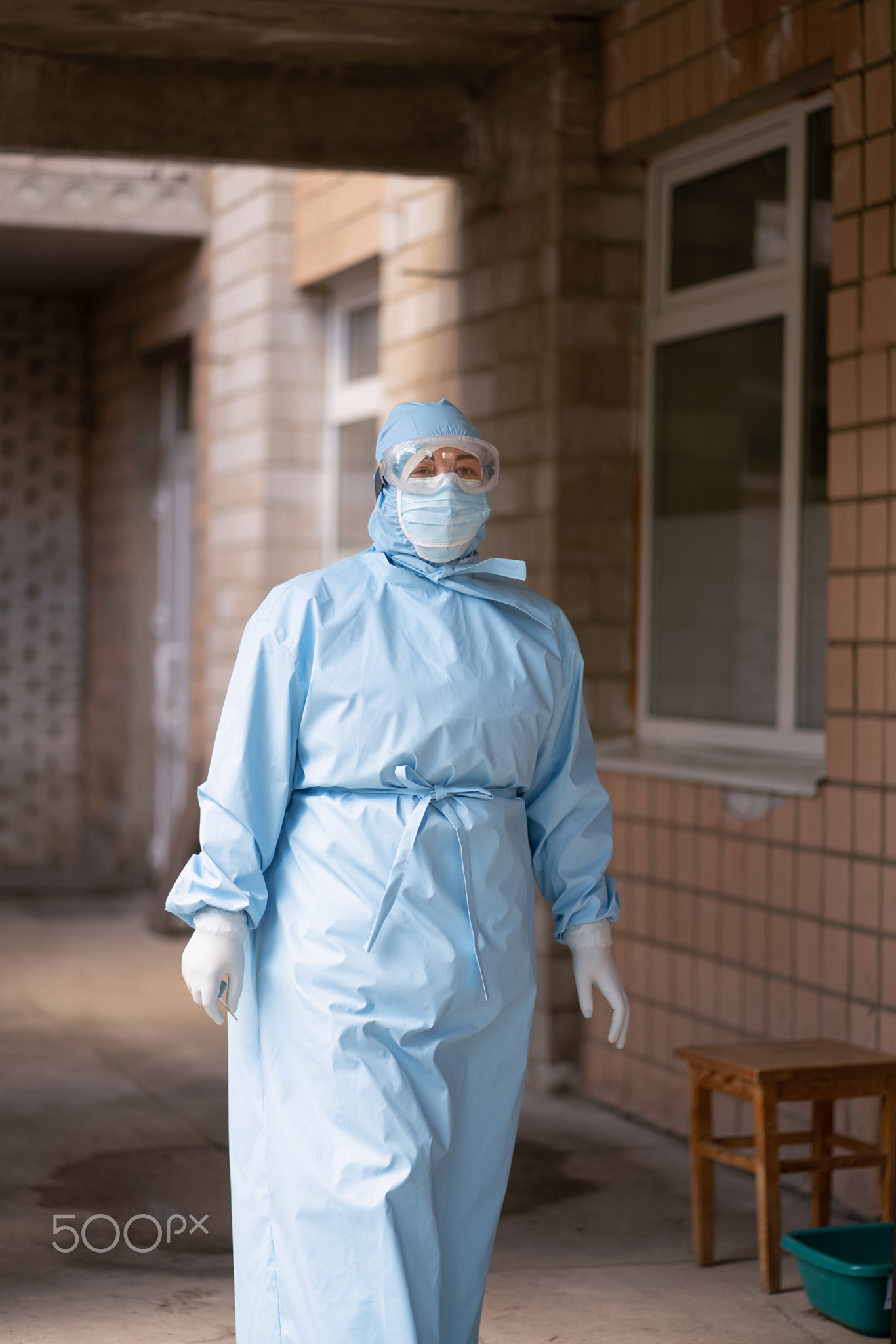 Female medic in protective suit, mask and goggles goes from the