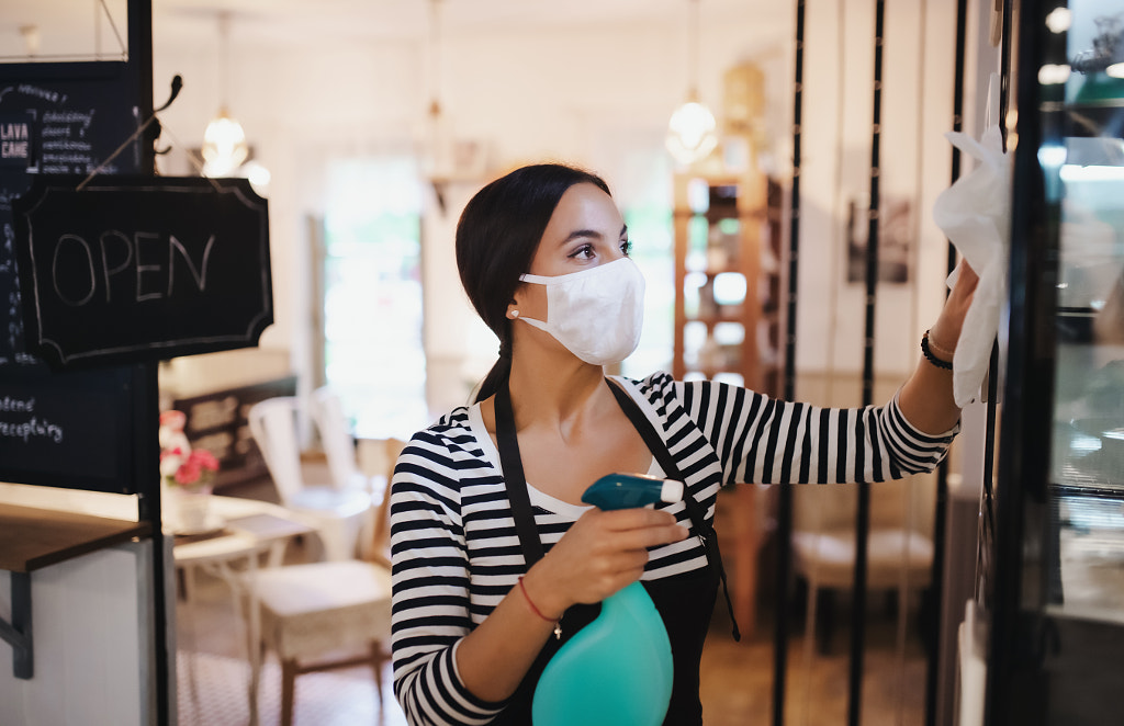 Young woman with face mask working indoors in cafe, disinfecting by Jozef Polc on 500px.com