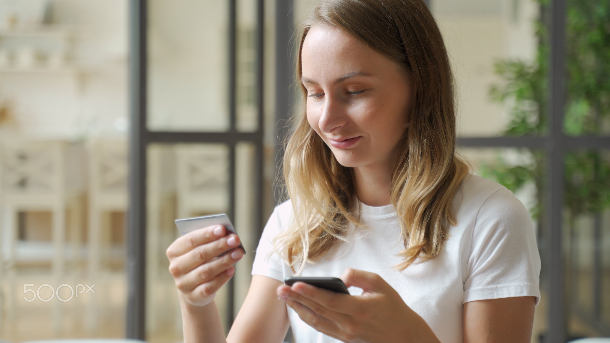 Woman holding credit card and smartphone. Young woman sitting on sofa