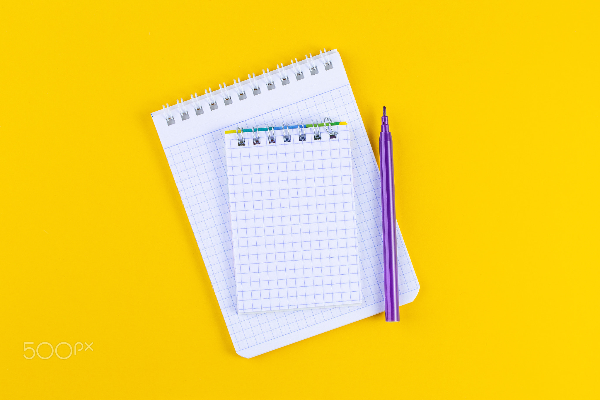 Open notebook on bright yellow paper background with pen.