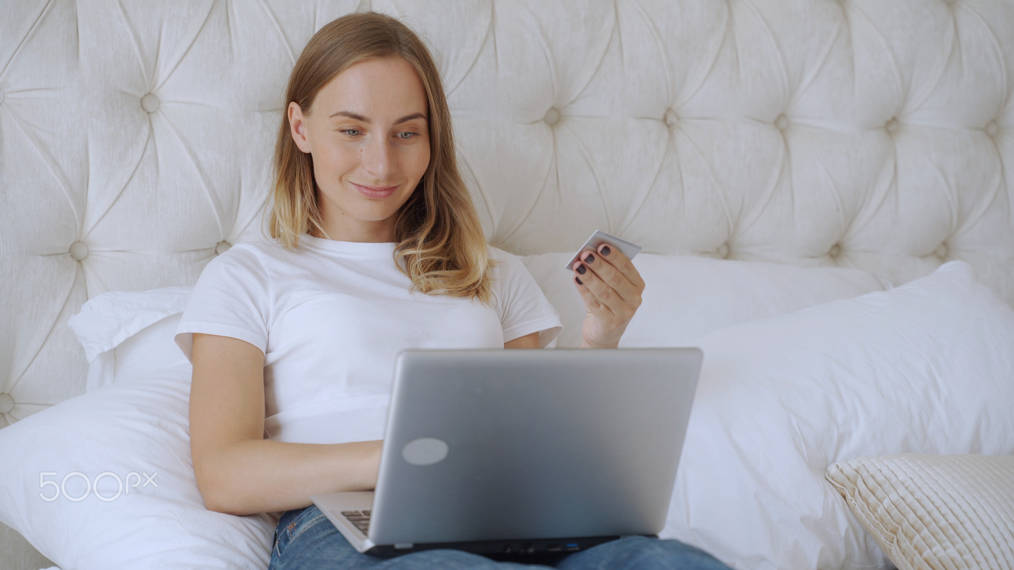 Woman holding credit card and using laptop, sitting on bed at home