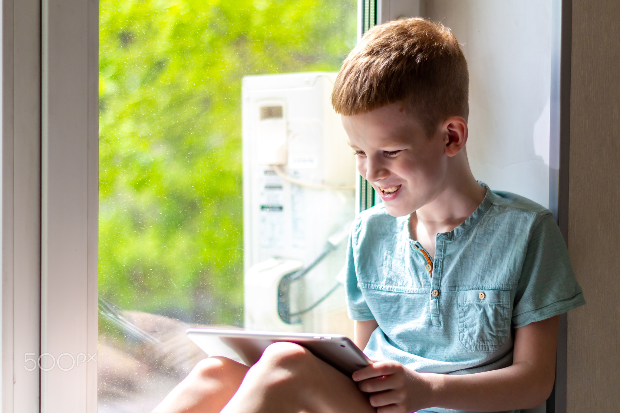 Young boy sitting on windowsill with tablet and play the games. Stay