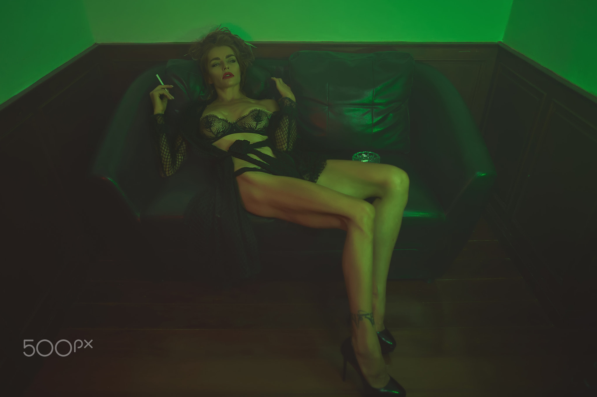 Beautiful long legged girl is posing on the couch in a green light