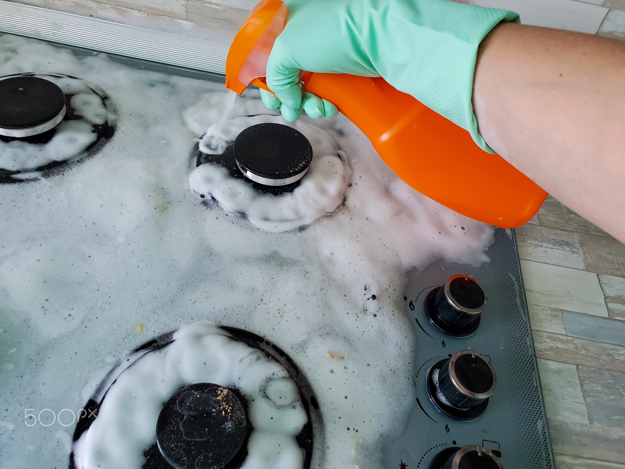 woman in rubber gloves uses a spray to wash a modern gas stove with a