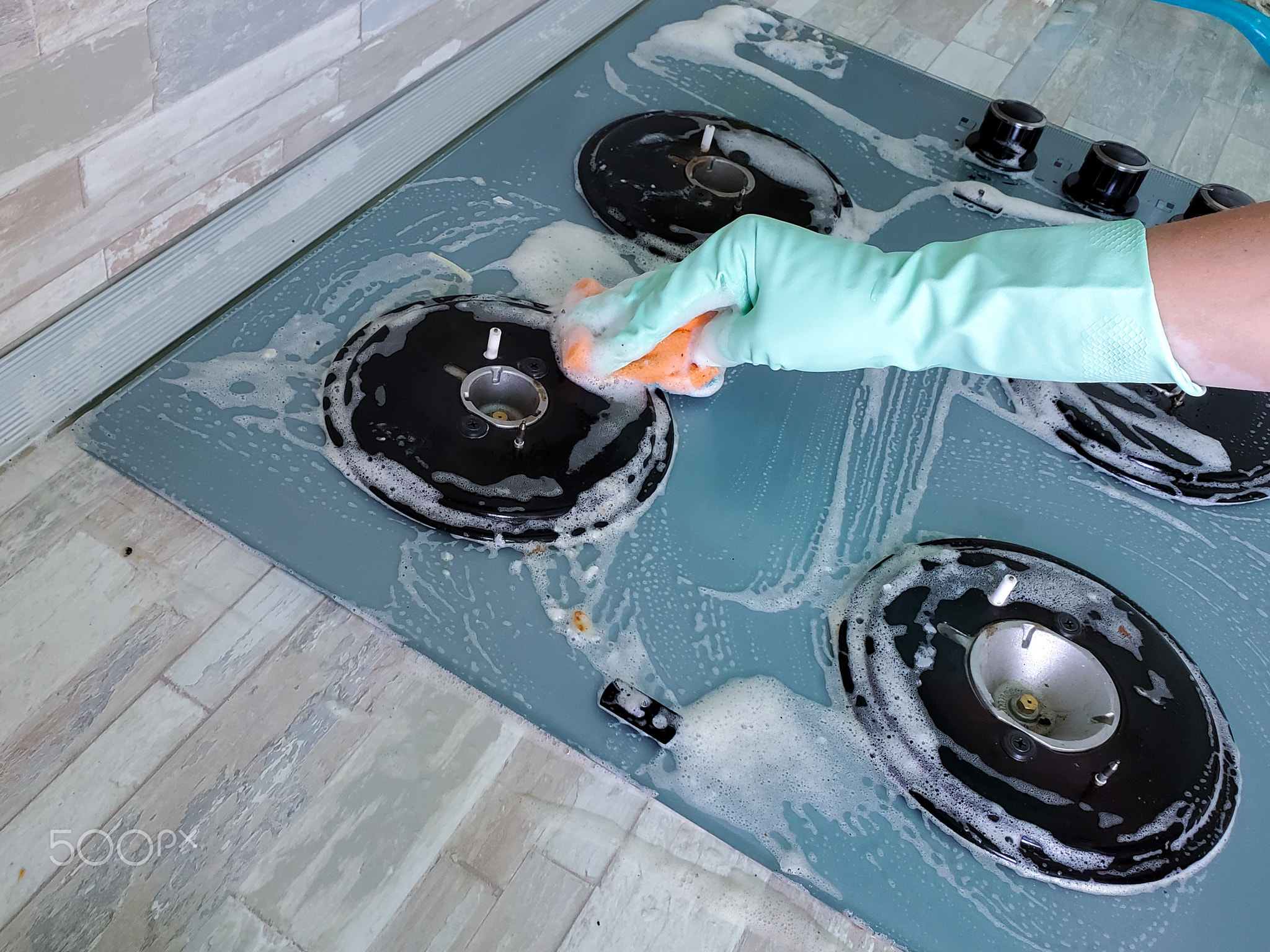 woman washes a glass-ceramic gas stove with a sponge and detergent