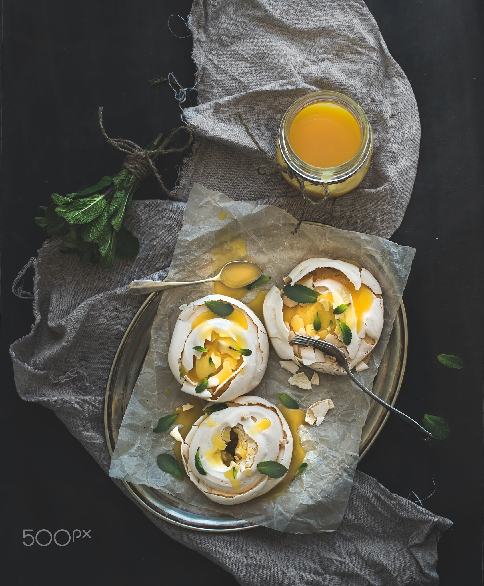 Merengues with lemon curd, fresh mint on silver tray, beige kitchen towel and grunge dark backdrop