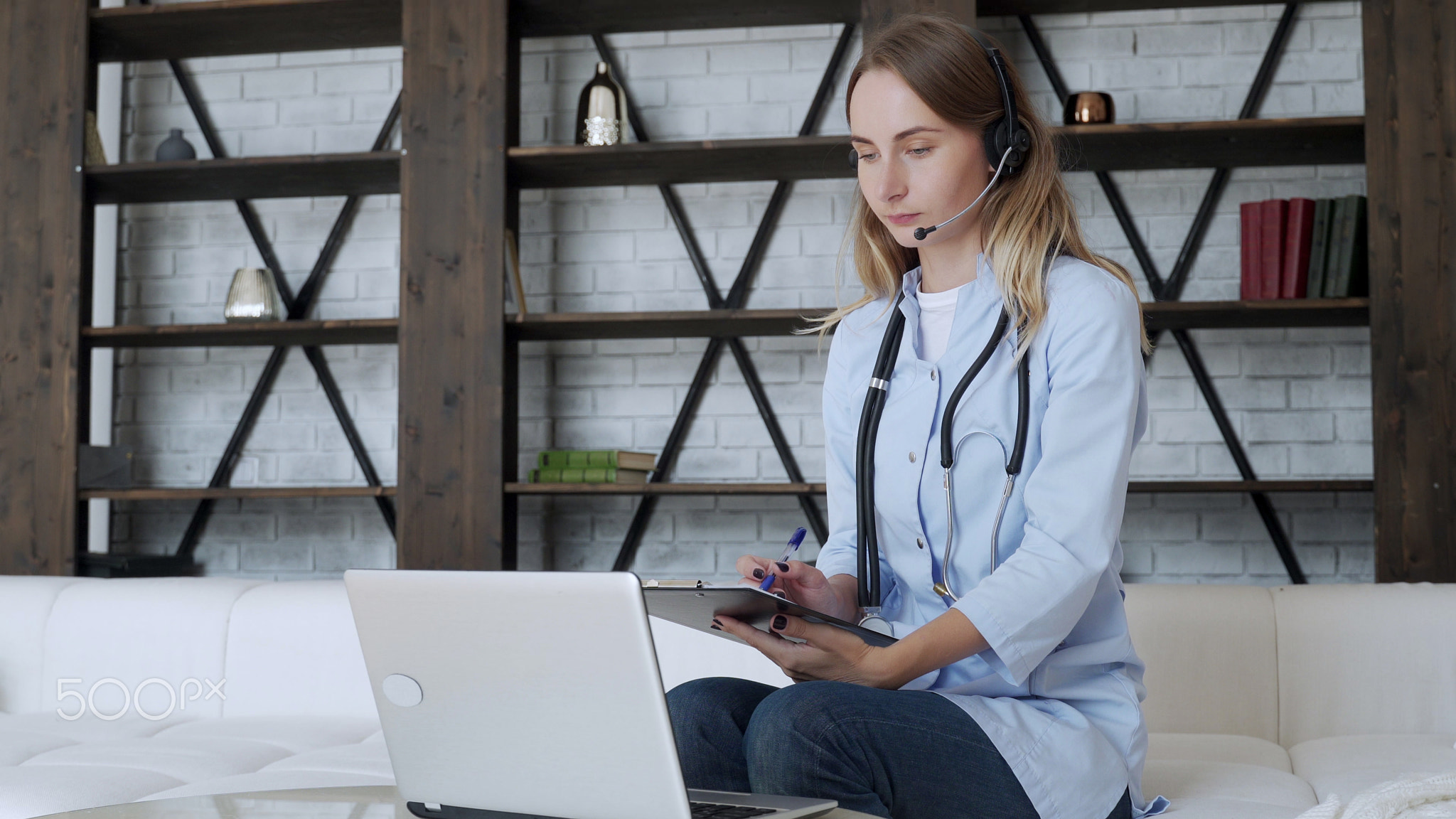 Woman wears a white coat and a headset while talking on a laptop