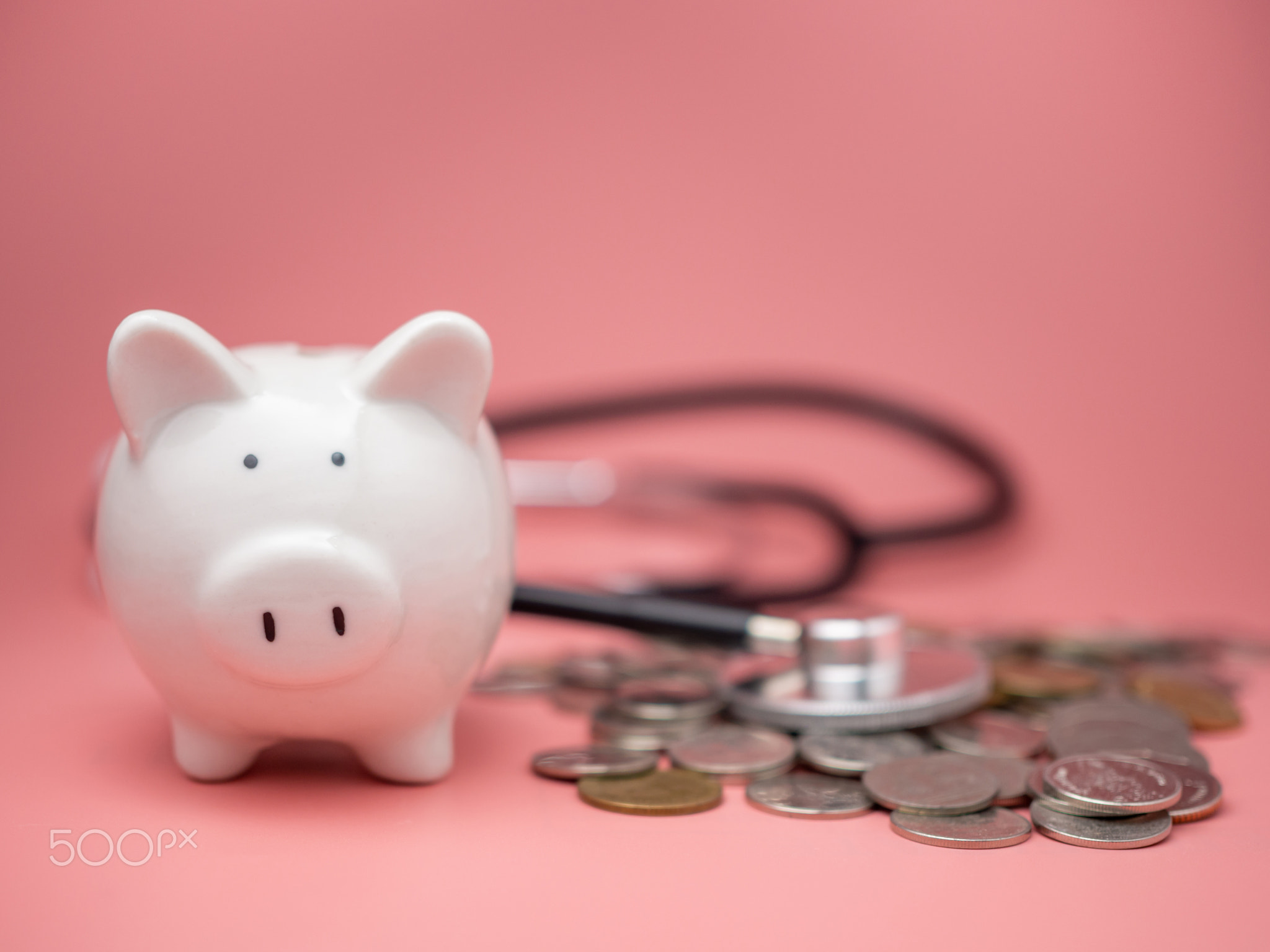 Stethoscope on the pile of money and piggy bank on pink background.