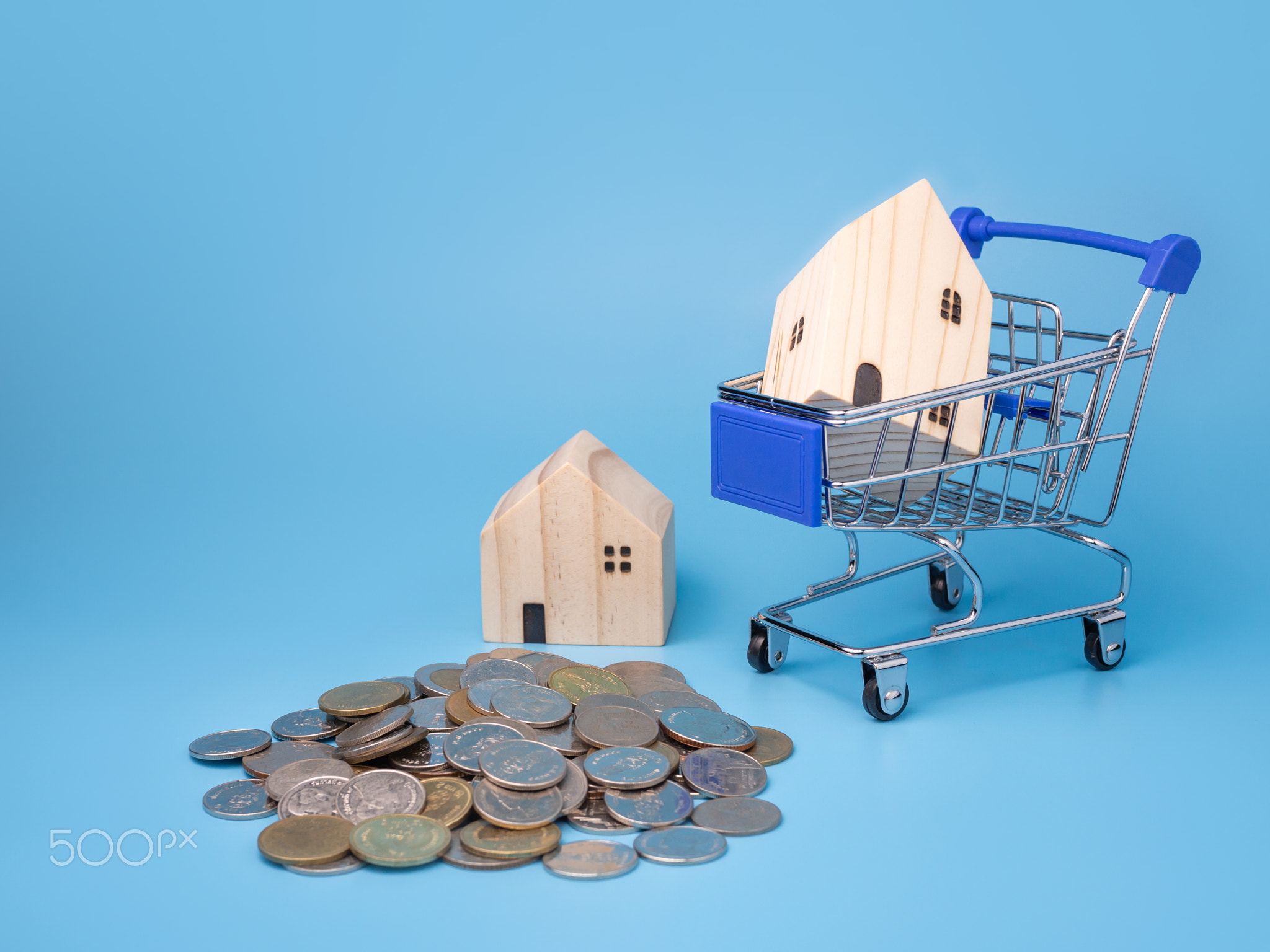 A model wooden house on a shopping cart With a pile of coins.