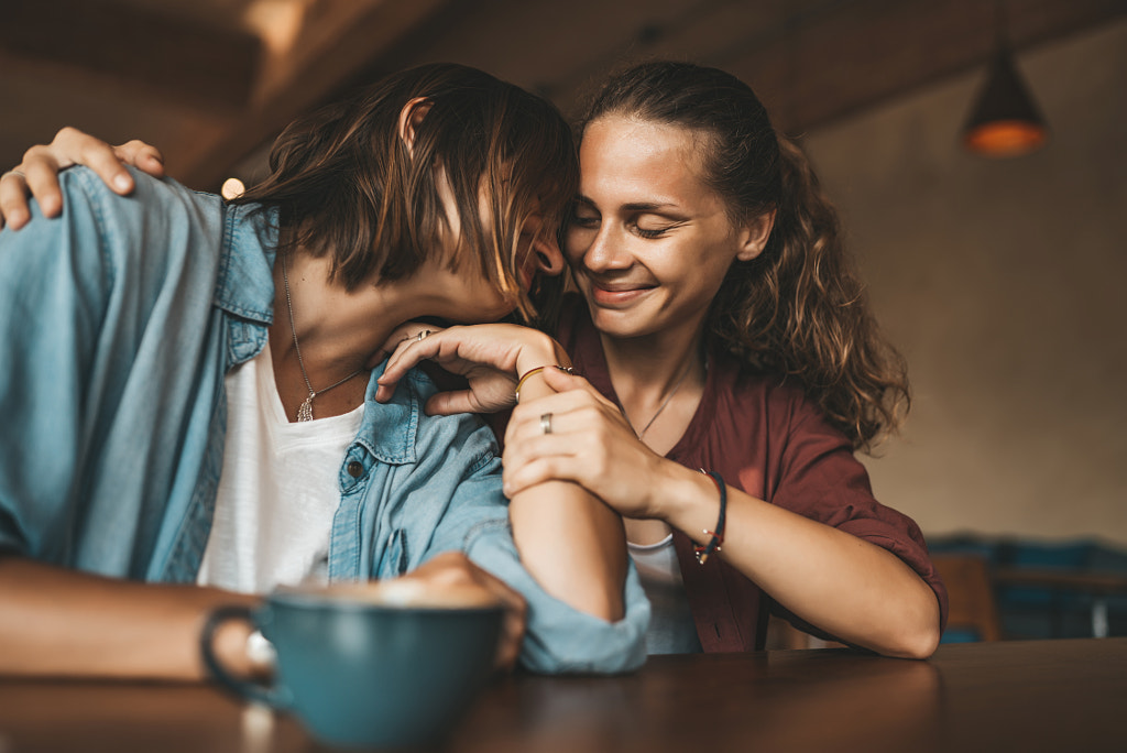 Lesbian couple hugging in cafe by Natalie Zotova on 500px.com