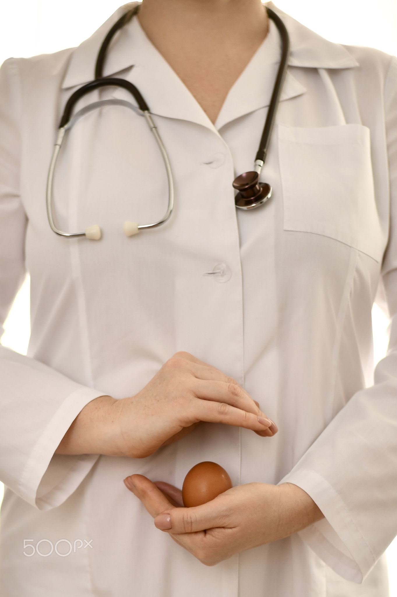 The doctor in a white robe, on one palm holds a chicken egg in the