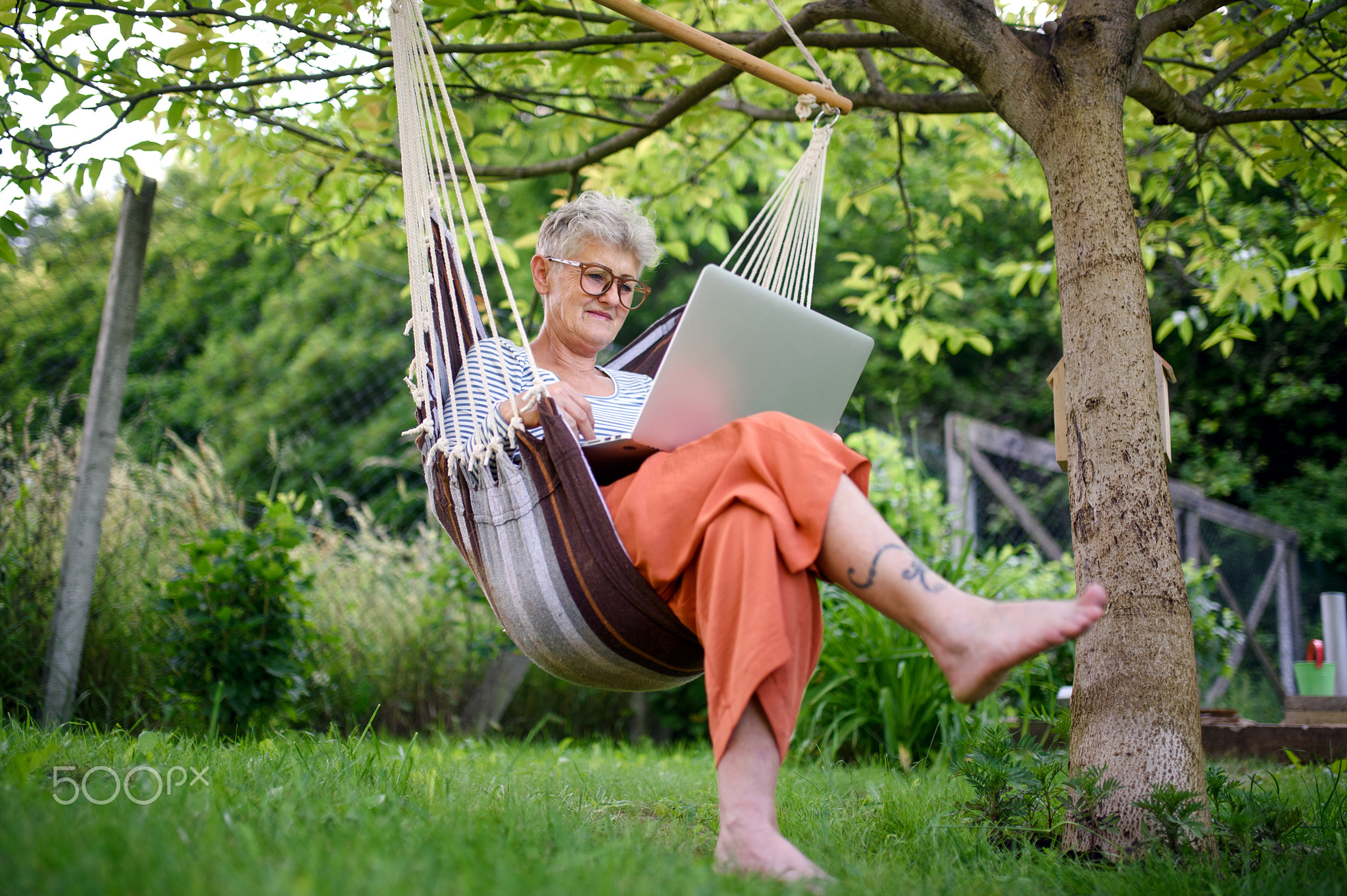 Portrait of active senior woman with laptop working outdoors in garden