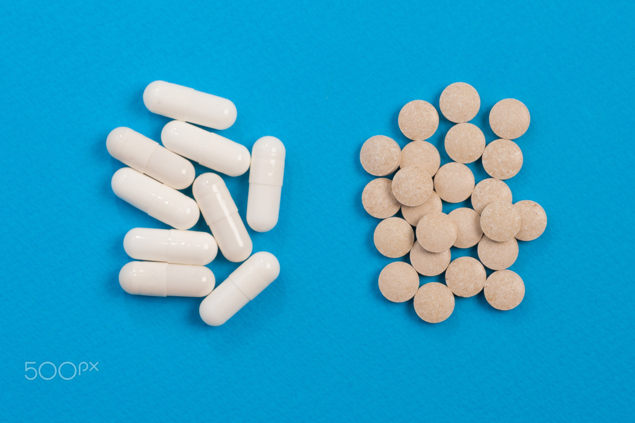 White capsules and brown tablets scattered on a blue background.