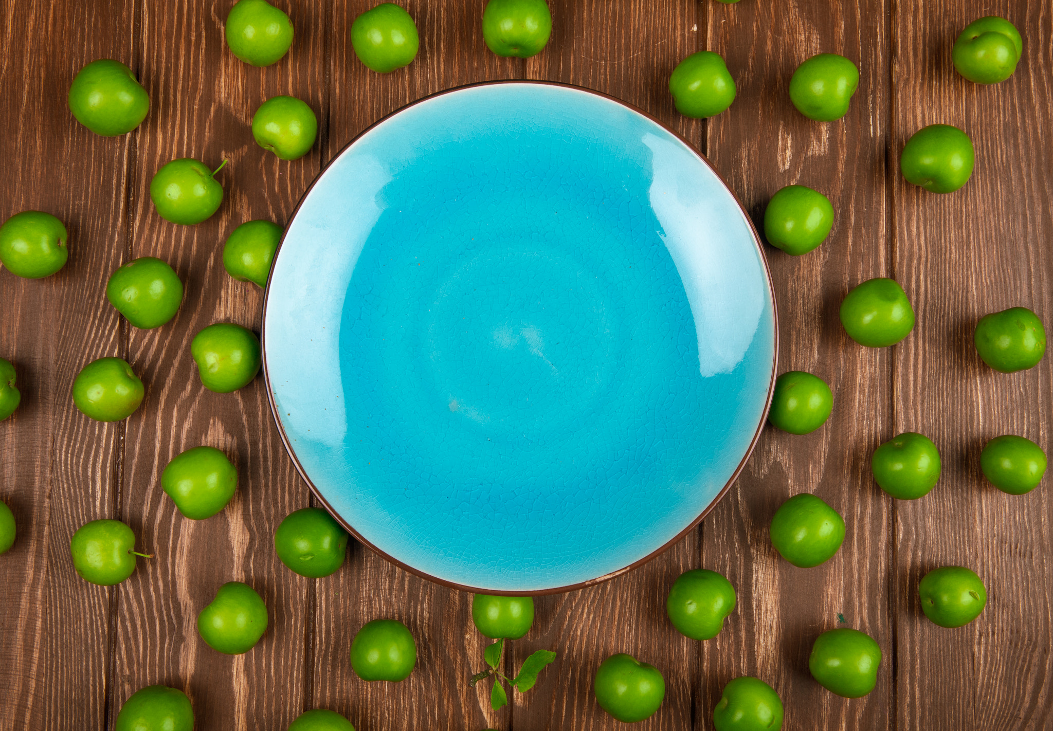 top view of an empty blue plate and sour green plums arranged ar