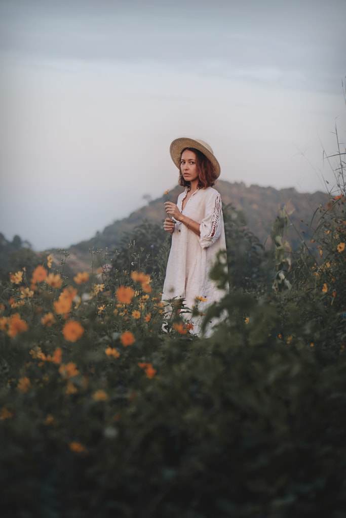 young woman in a linen dress and straw hat sits on a viewpoint in the by Roma Black on 500px.com