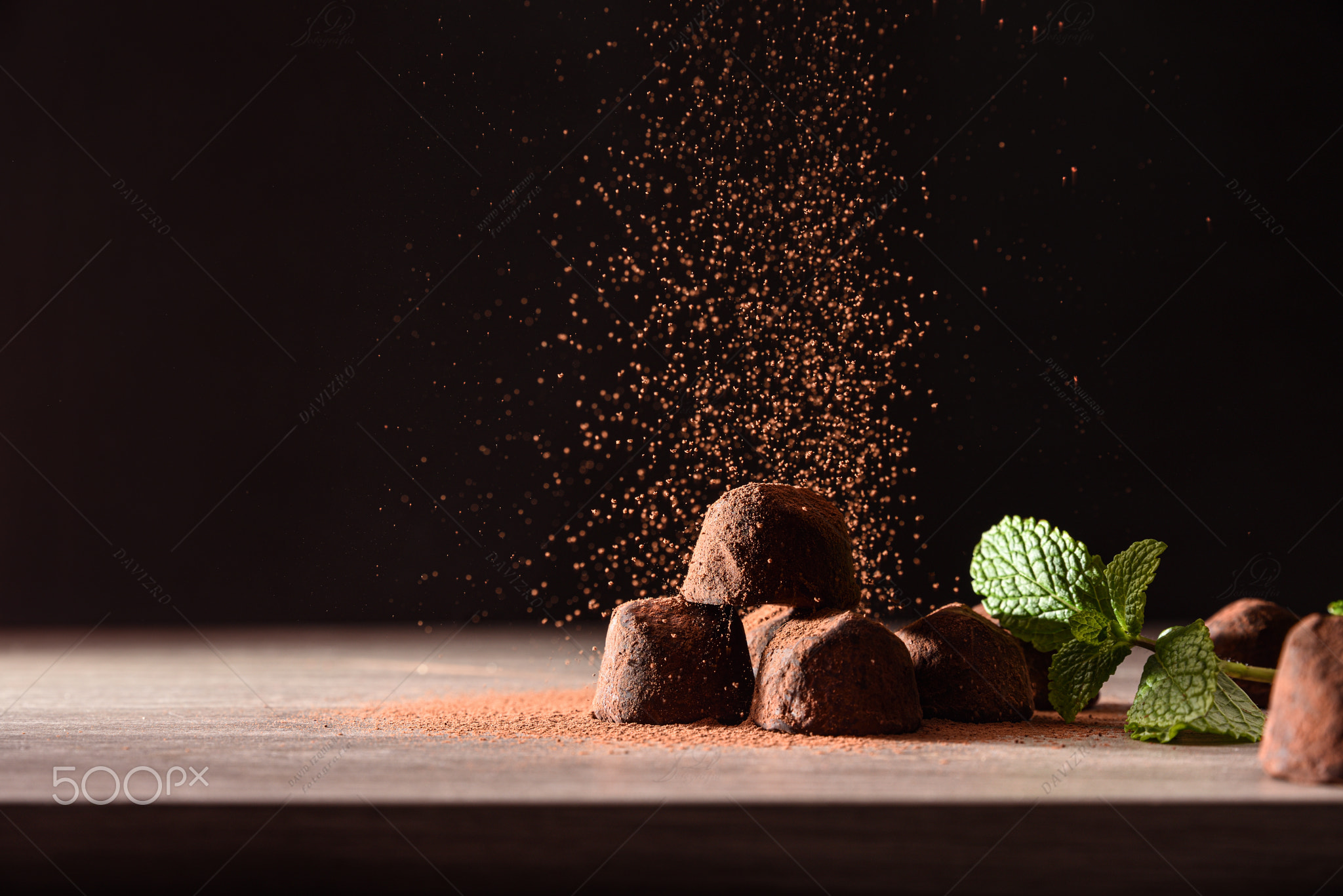 Chocolate truffles with mint leaves on table falling cocoa powder