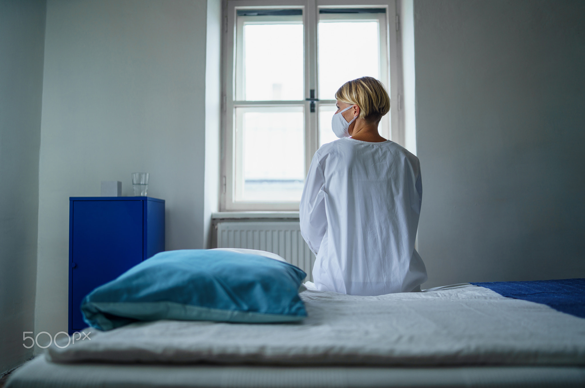 Rear view of woman patient sitting on bed in hospital feeling stressed