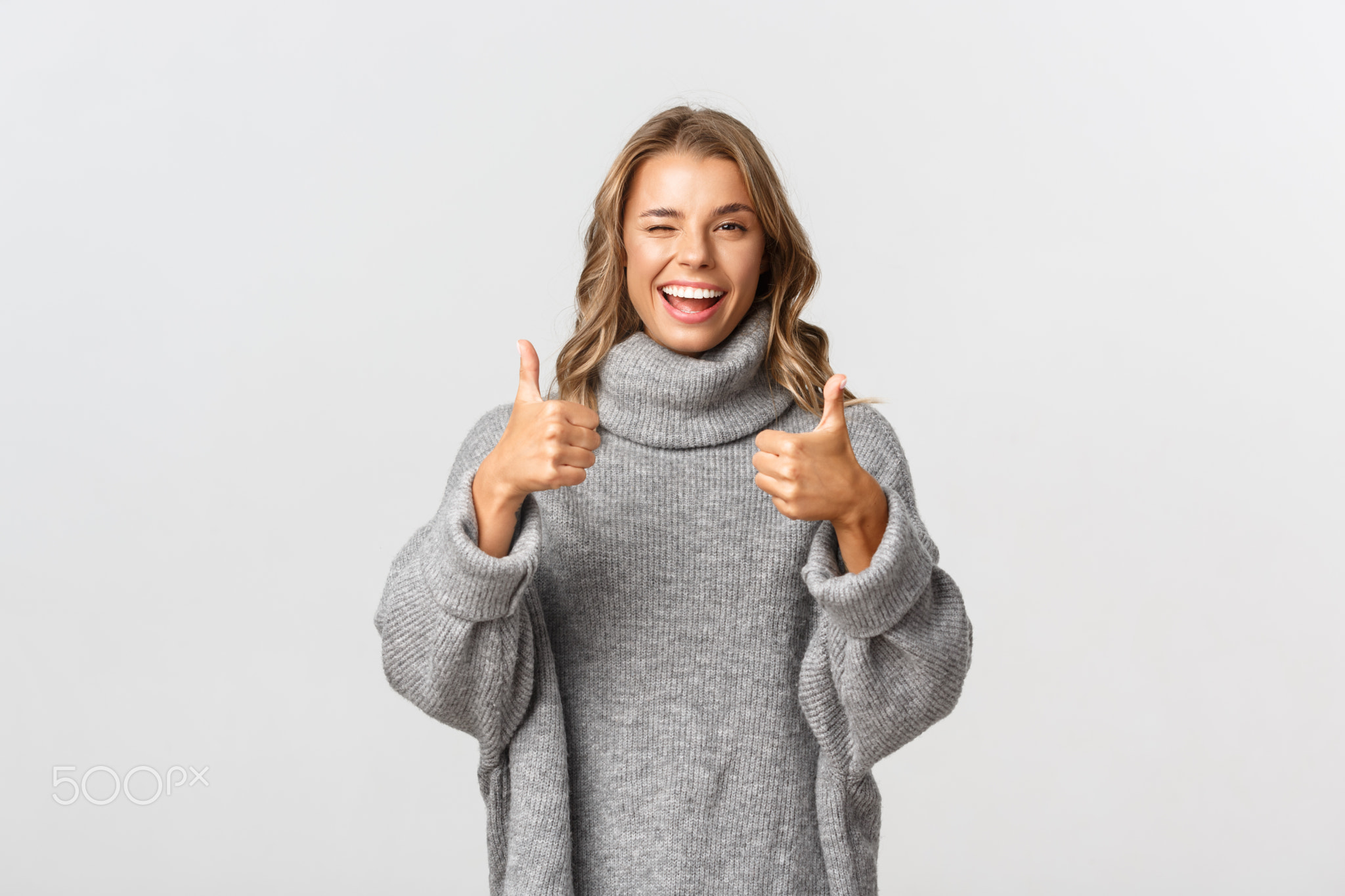 Image of attractive confident woman in grey sweater, showing thumbs-up