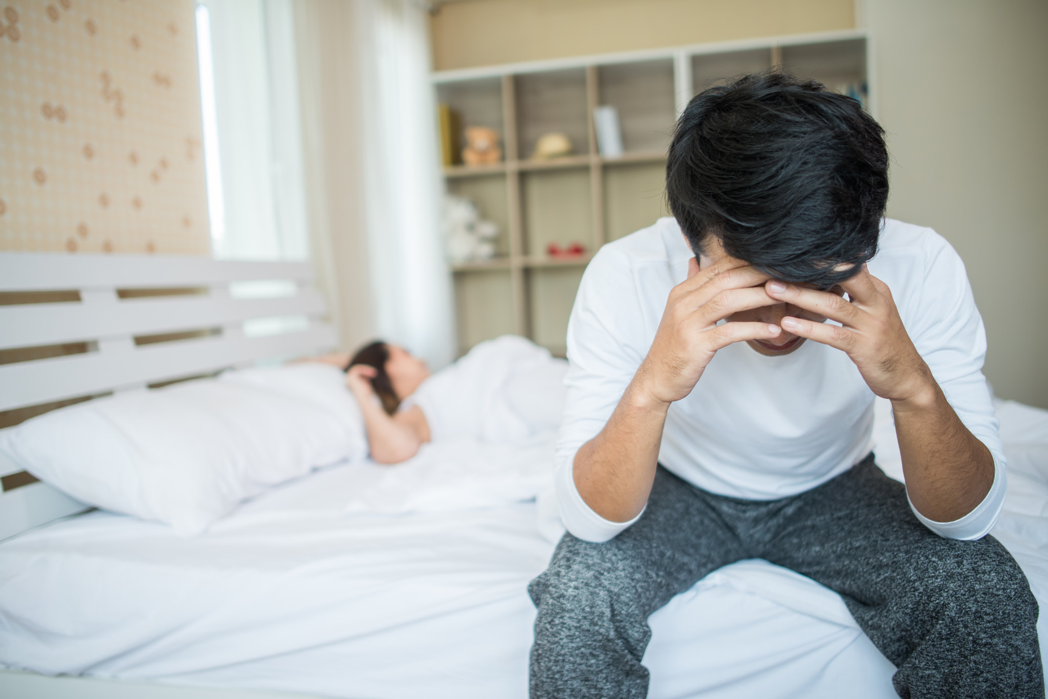 Upset man having problem sitting on the bed after arguing.