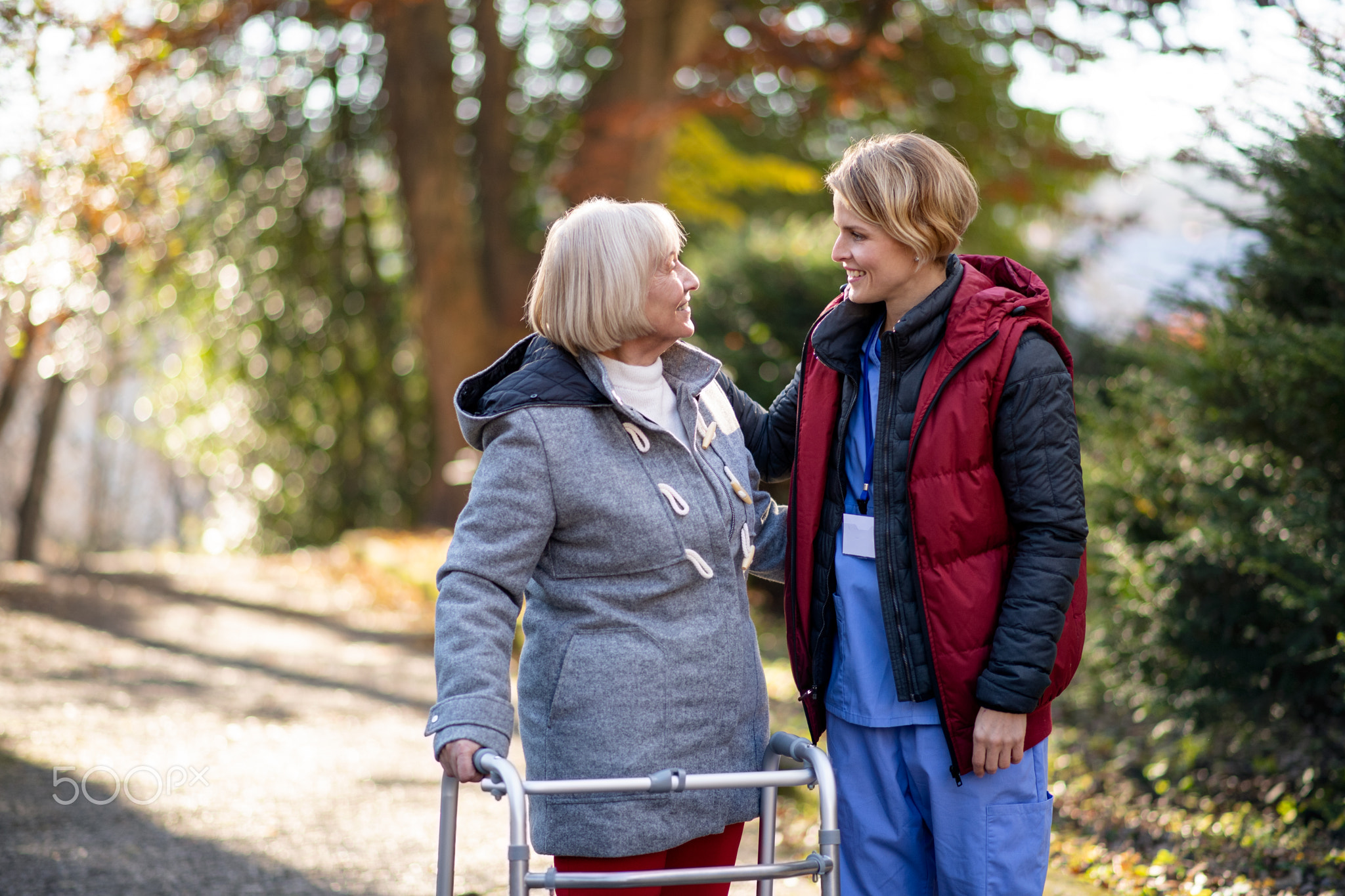 Senior woman with walking frame and caregiver outdoors on a walk in