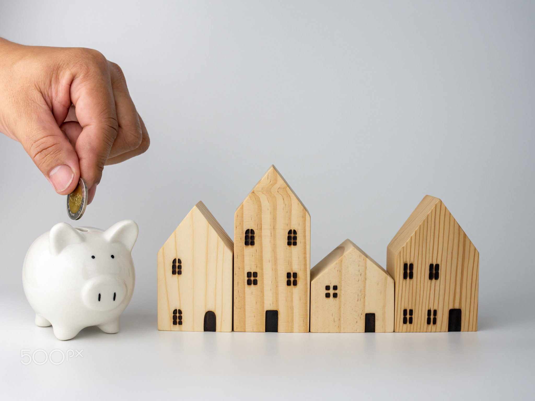 A model wooden house and a man's hand holding a coin .