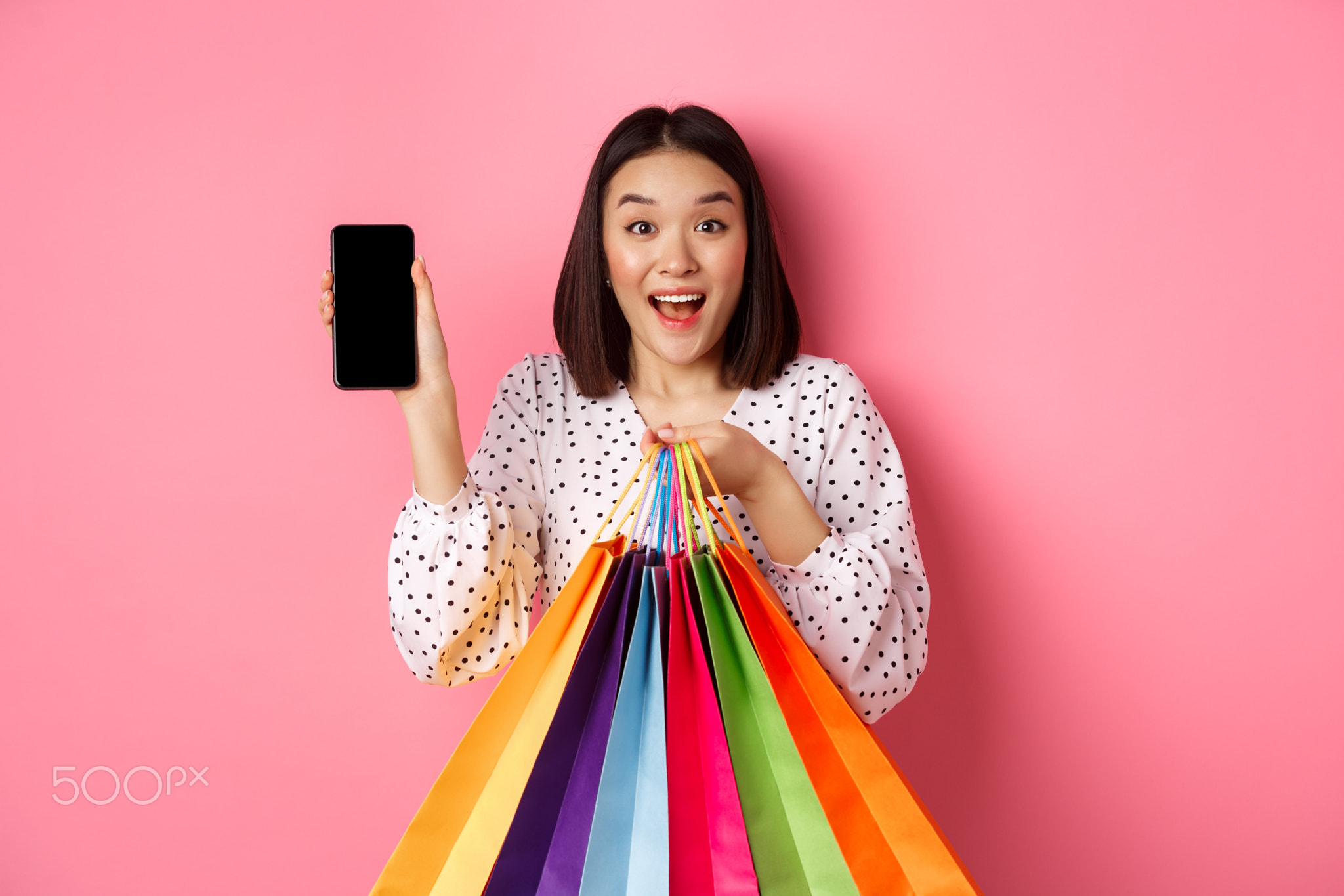 Attractive asian woman showing smartphone app and shopping bags