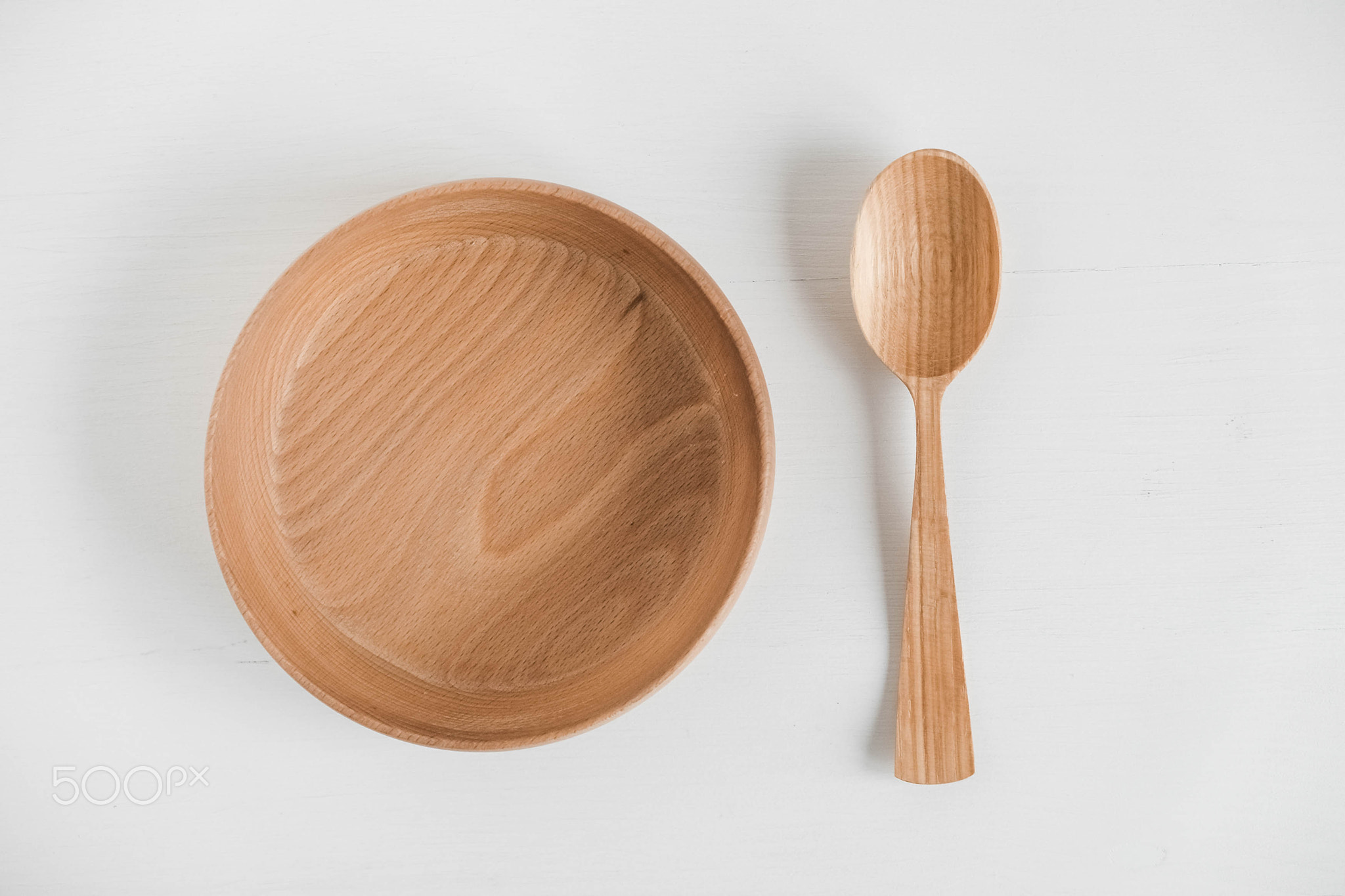 Empty wooden bowl and wooden spoon on a white background. Top view