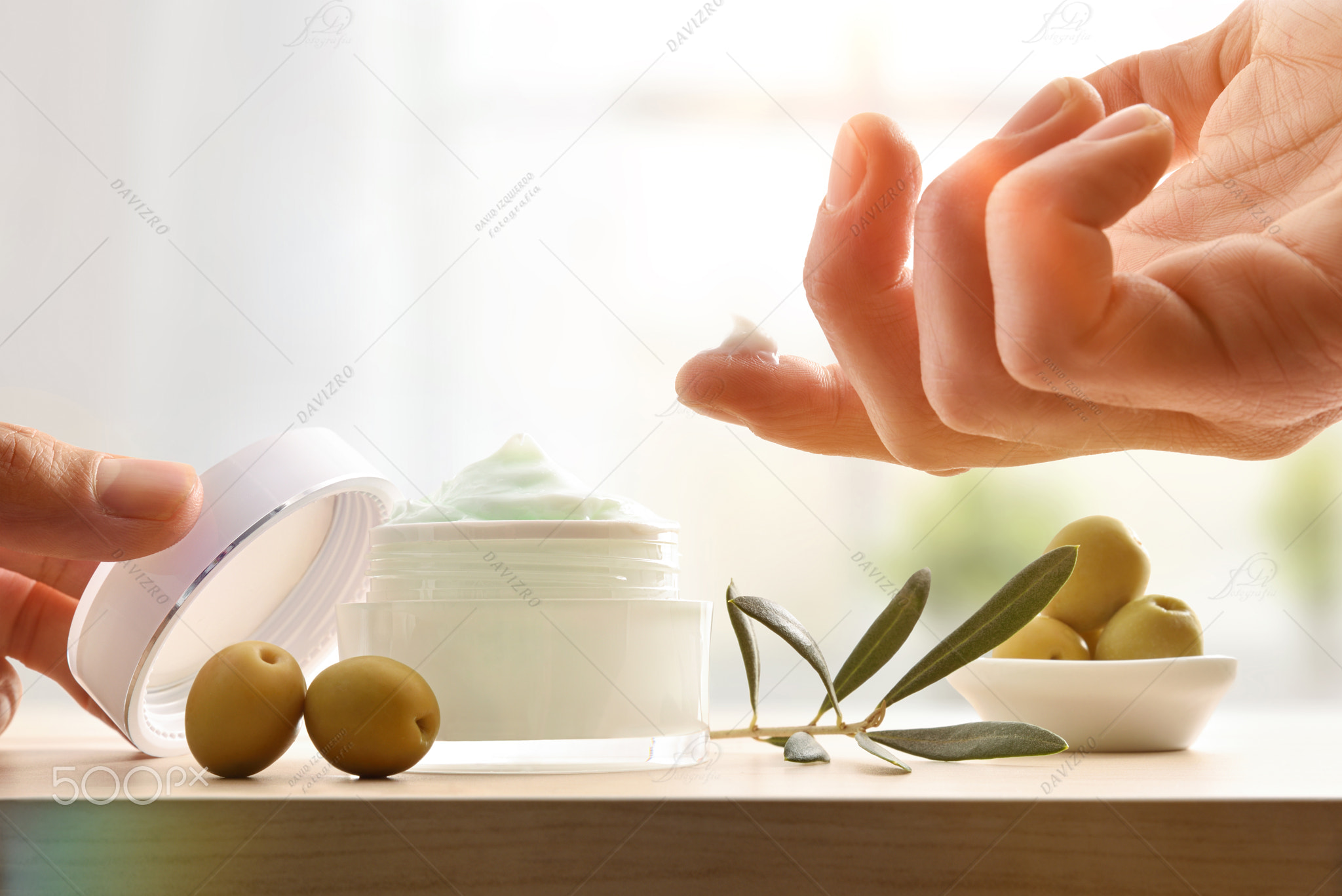 Hands taking sample of olive body cream on wooden table