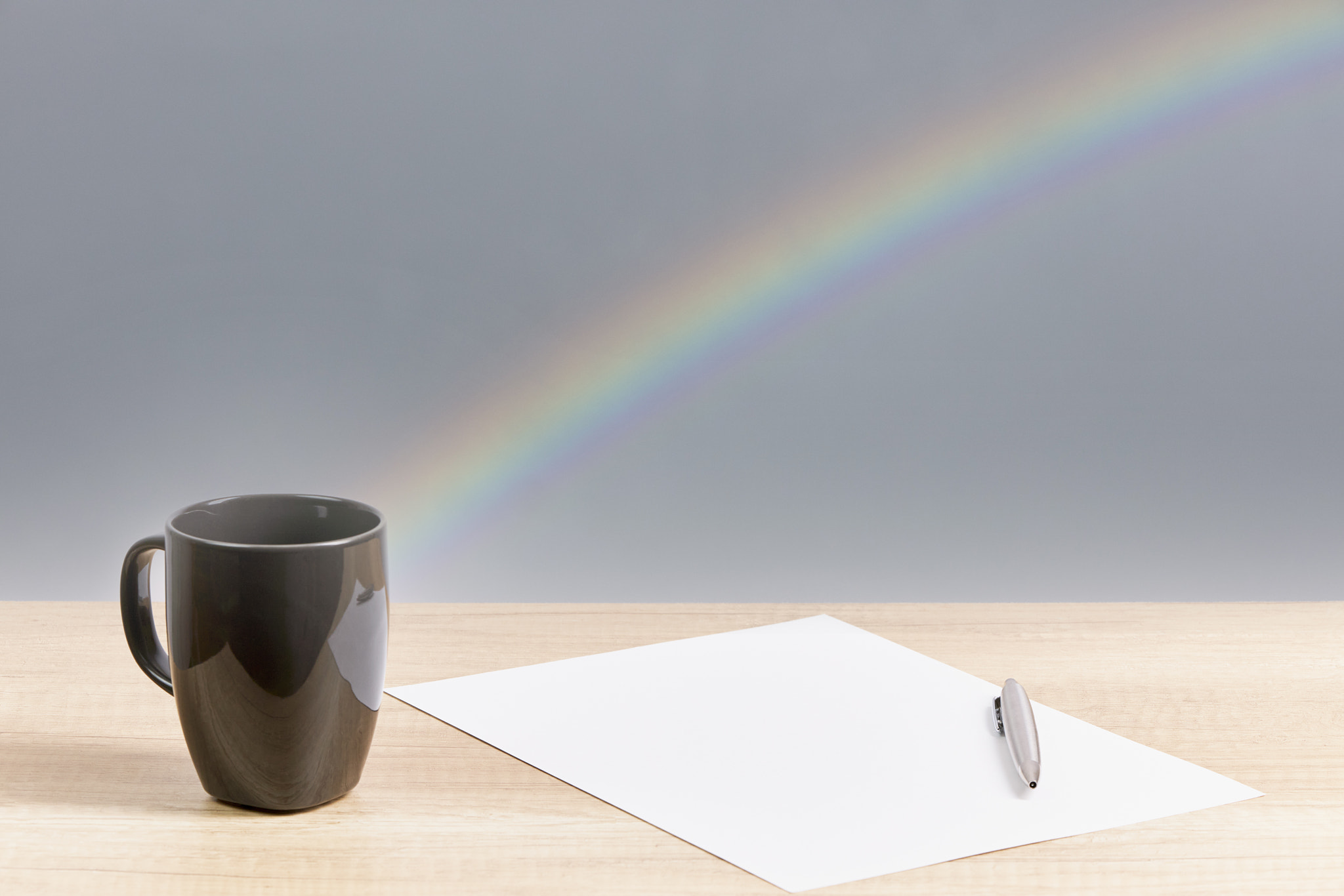 Pen on a paper, next to a cup and with the background of a rainbow