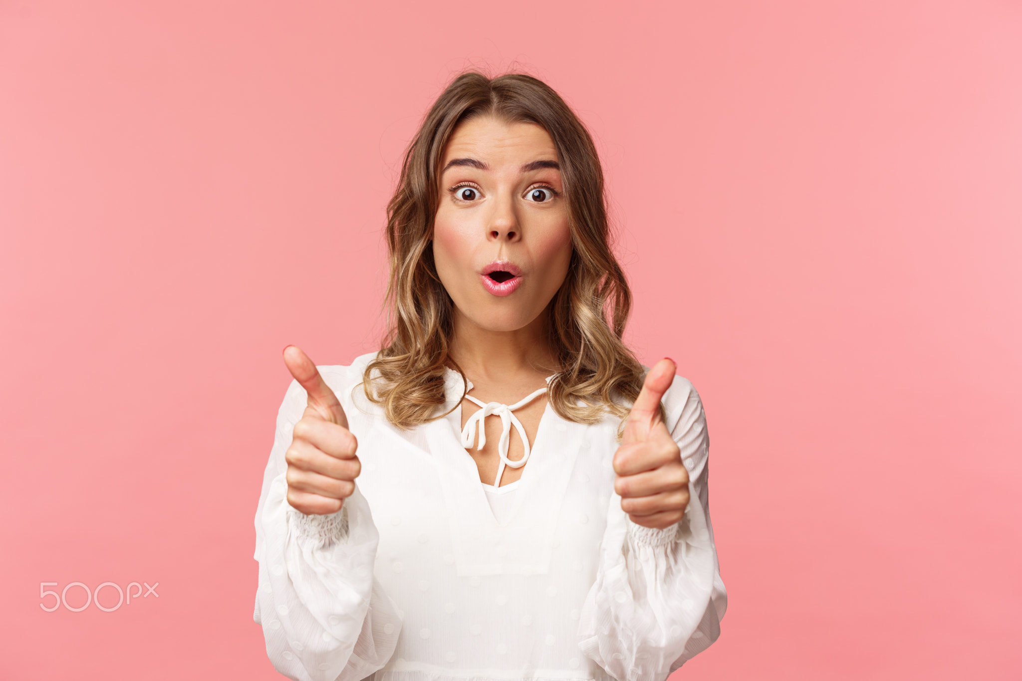 Close-up portrait of impressed blond girl showing thumbs-up look