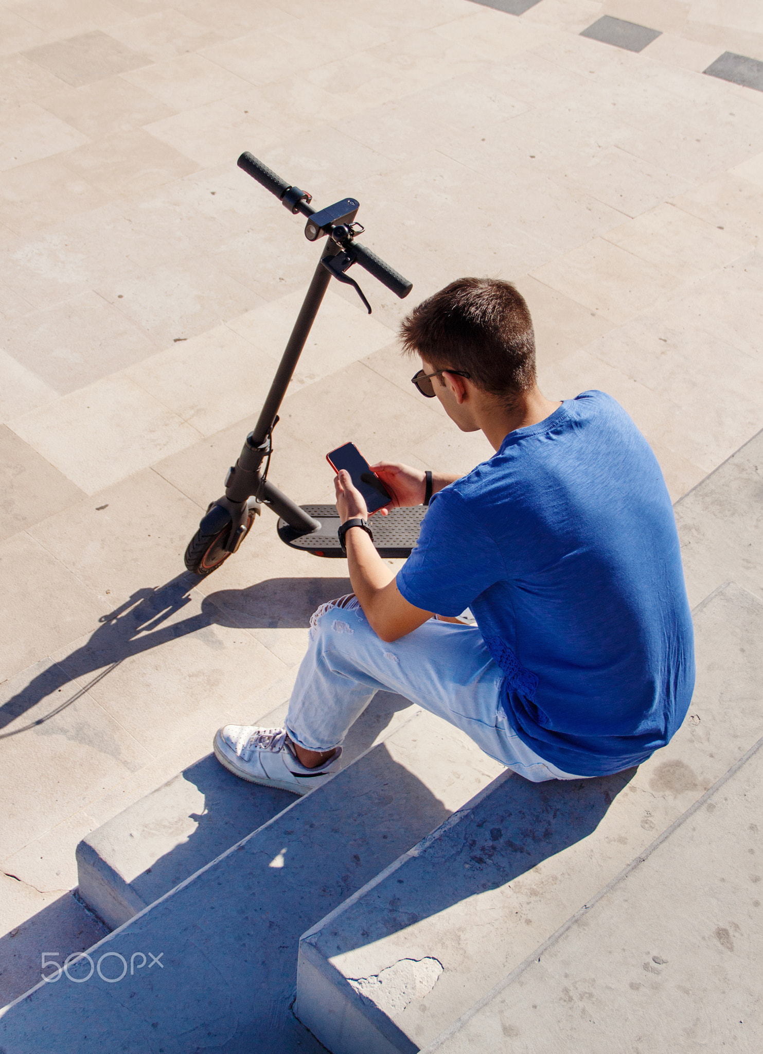 Young Caucasian man sitting outdoor near electric scooter