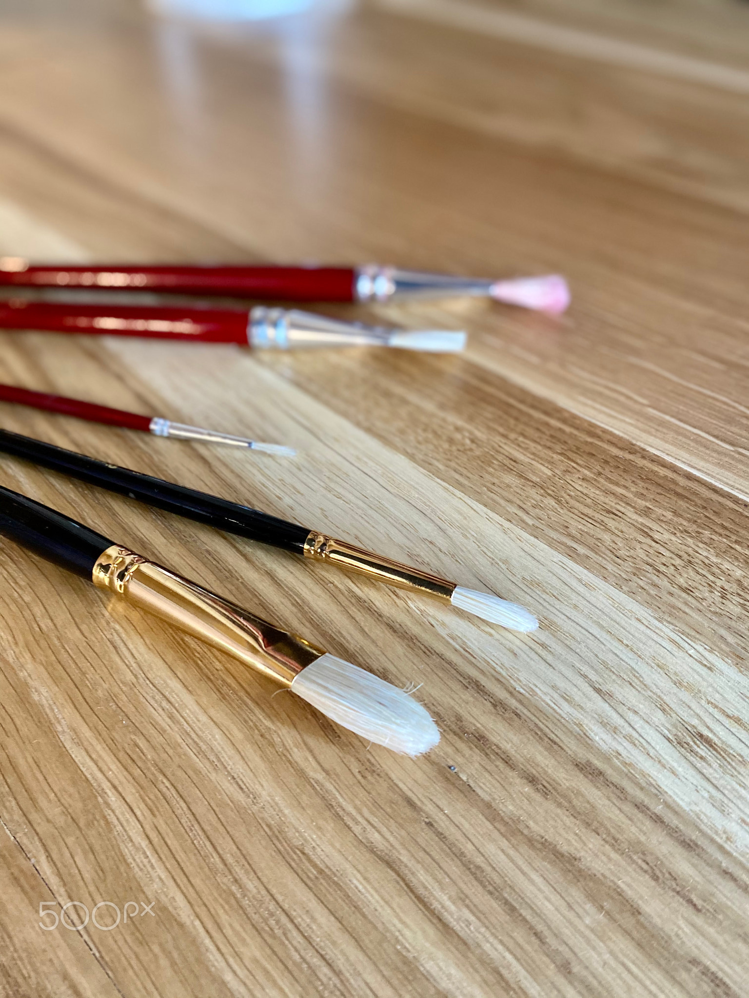 A group of brushes lies on a wooden table.