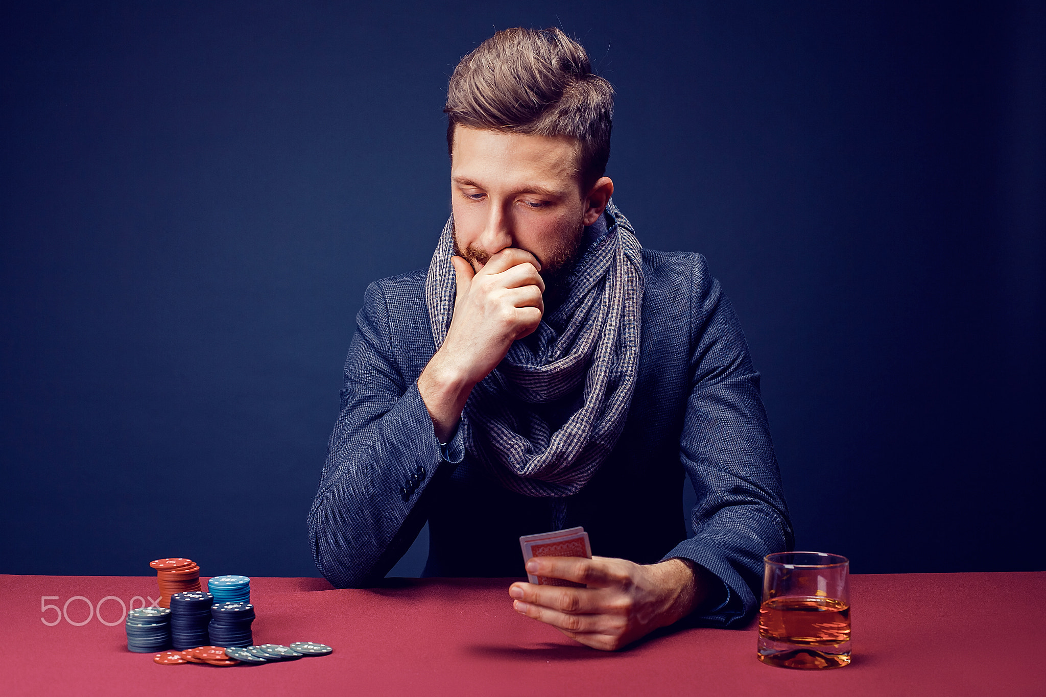 Stylish bearded Man in suit and scarf playing in dark casino, smoking