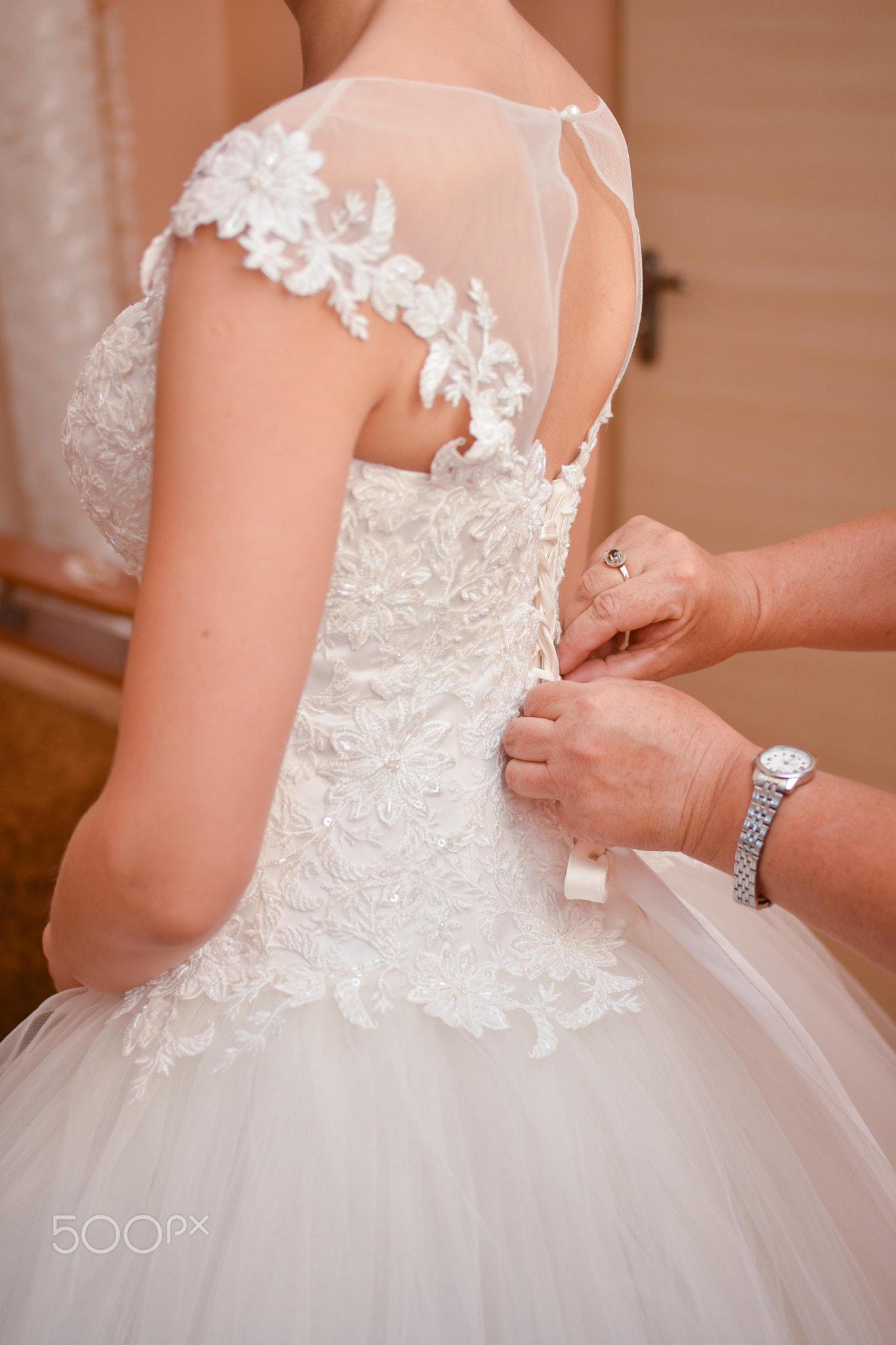 The hands of an adult woman fasten the bride's dress.