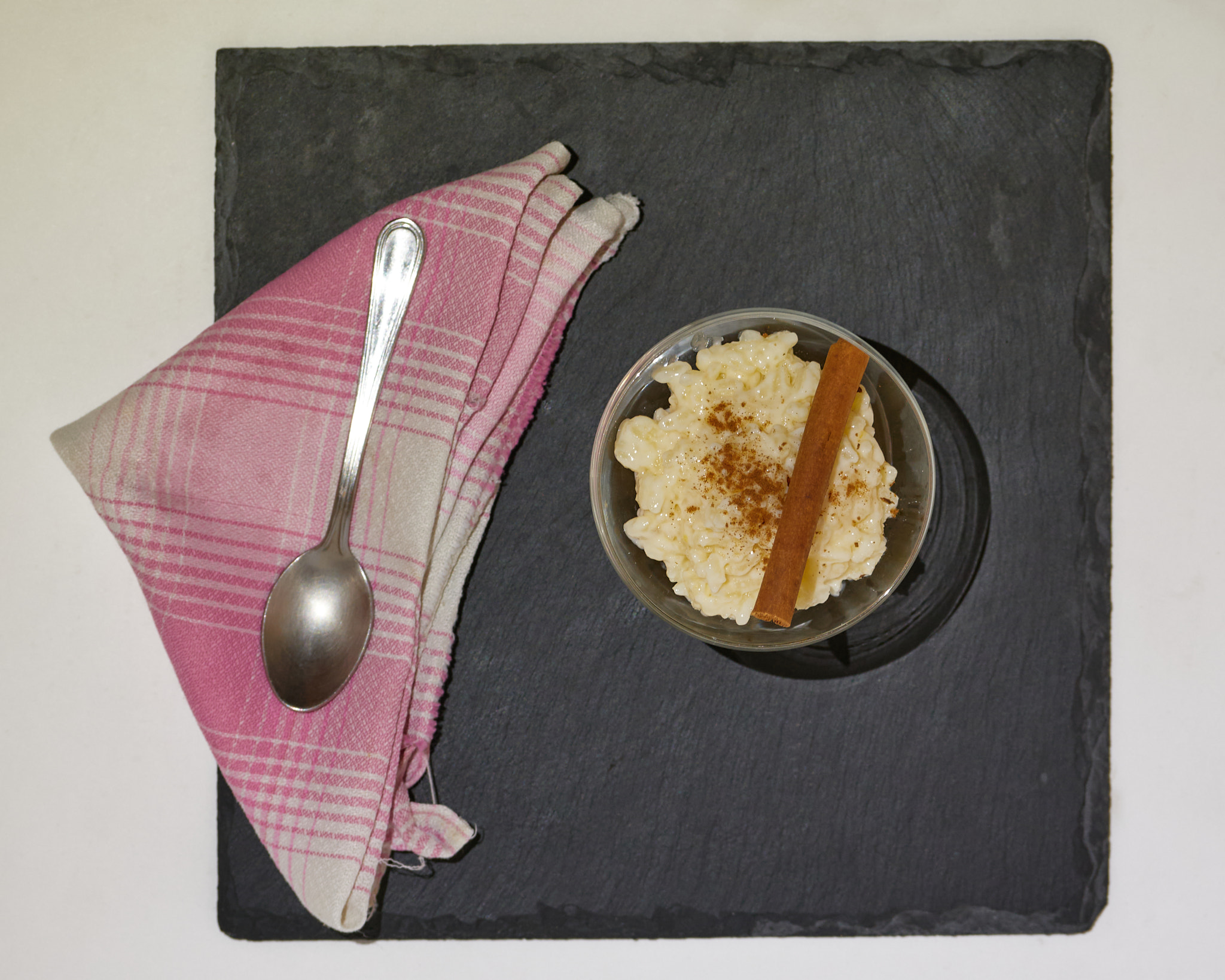 Rice pudding glass with cinnamon stick on black slate board. Top View