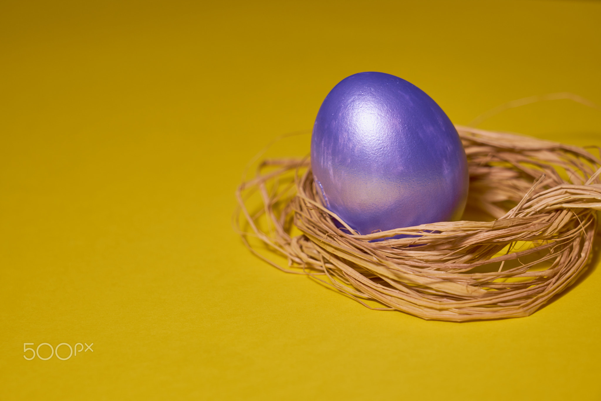 Pearl colored egg in the nest on a yellow background.