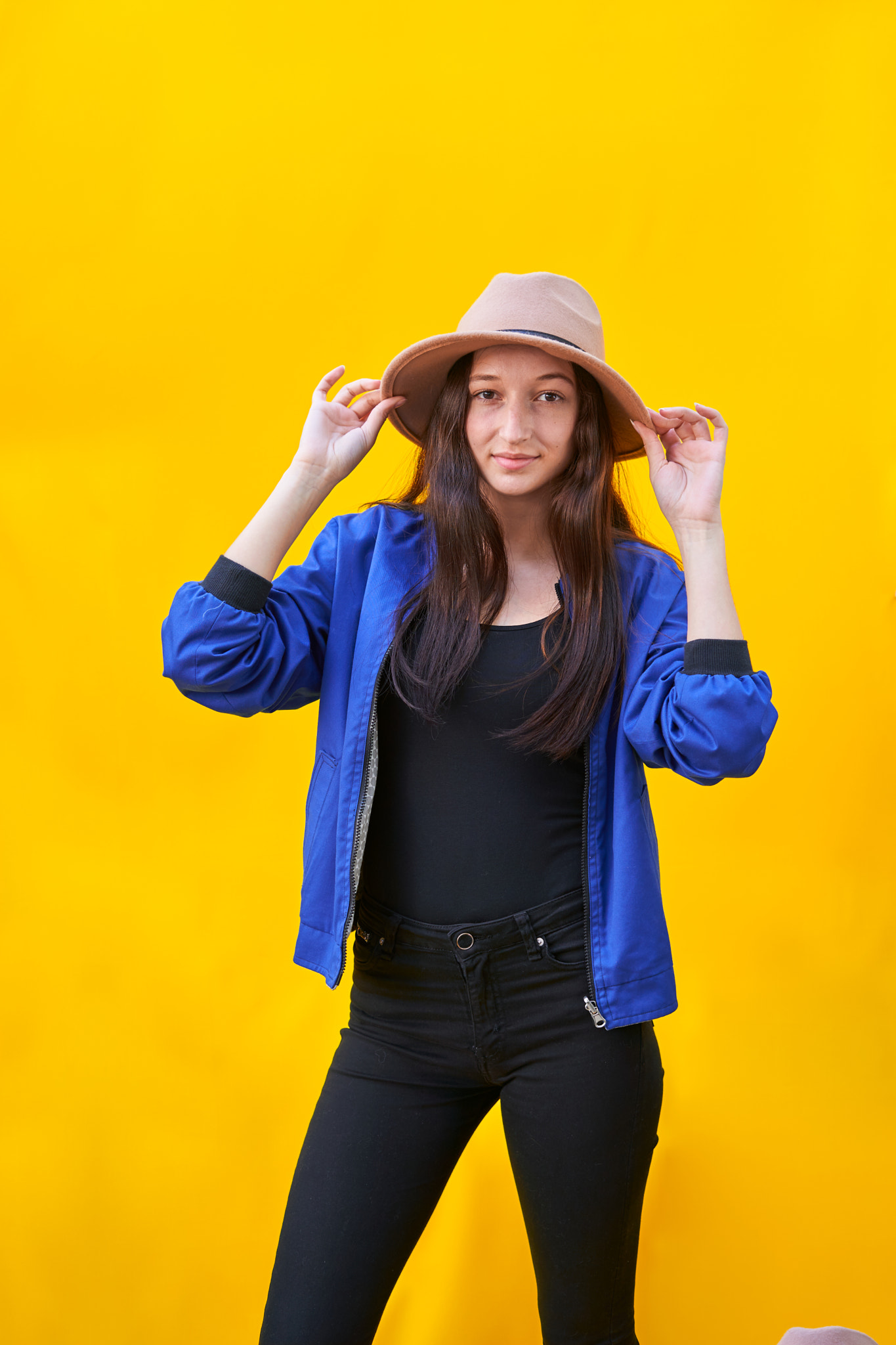 Young caucasian woman on yellow background, holding hat with hand