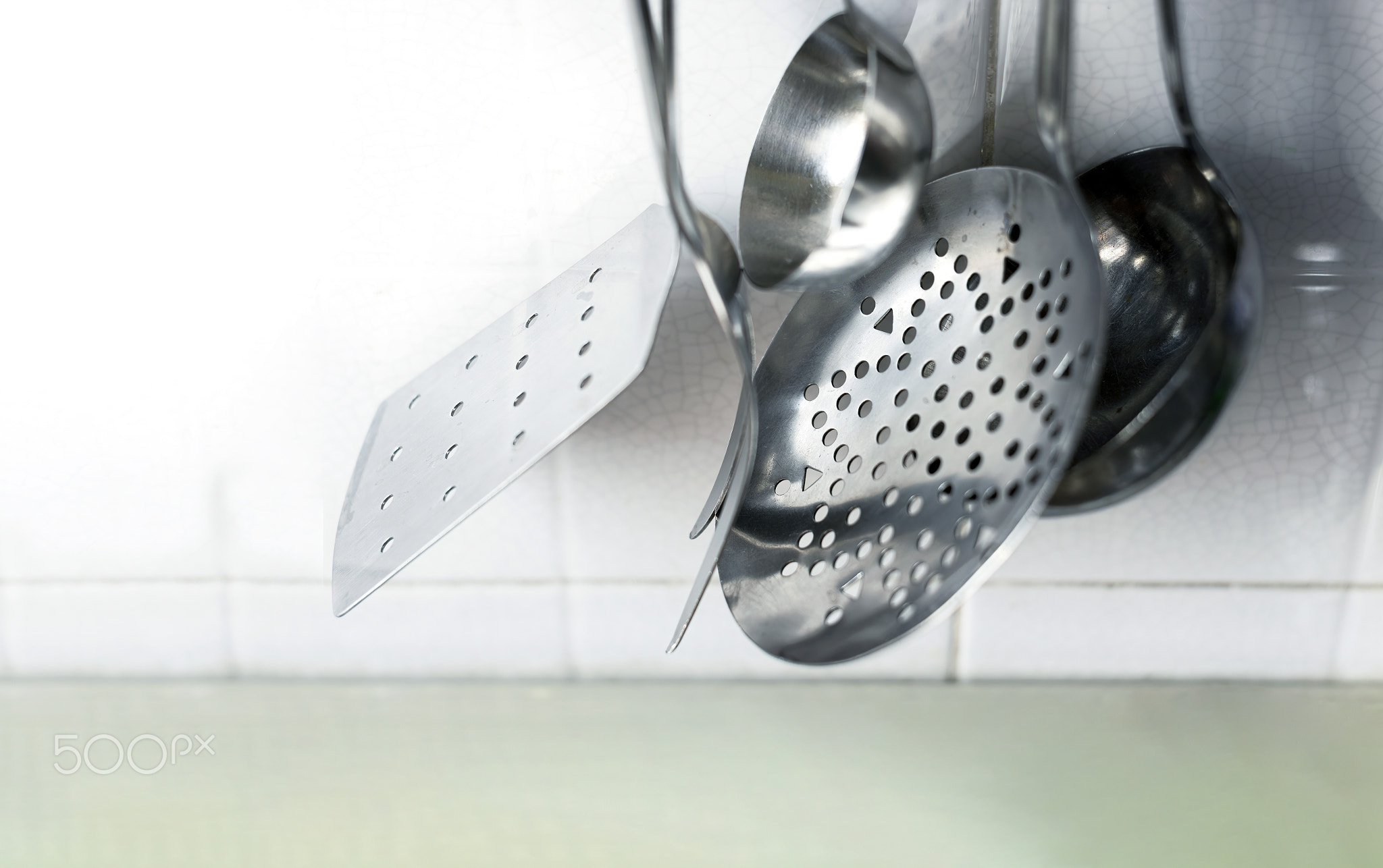 Metal kitchen utensils hanging on the tiled kitchen wall