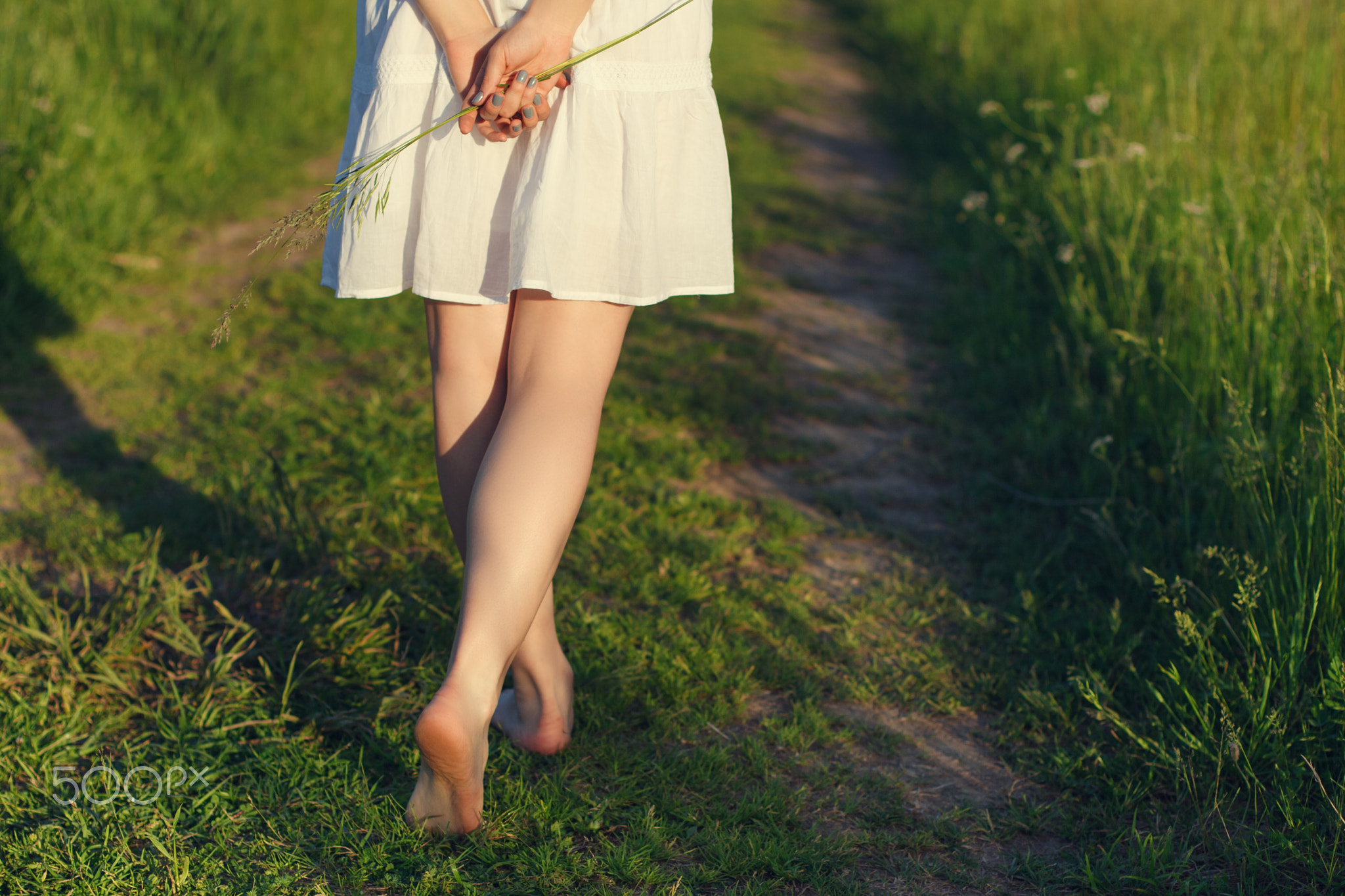 The bare feet of a girl walking on the green grass.