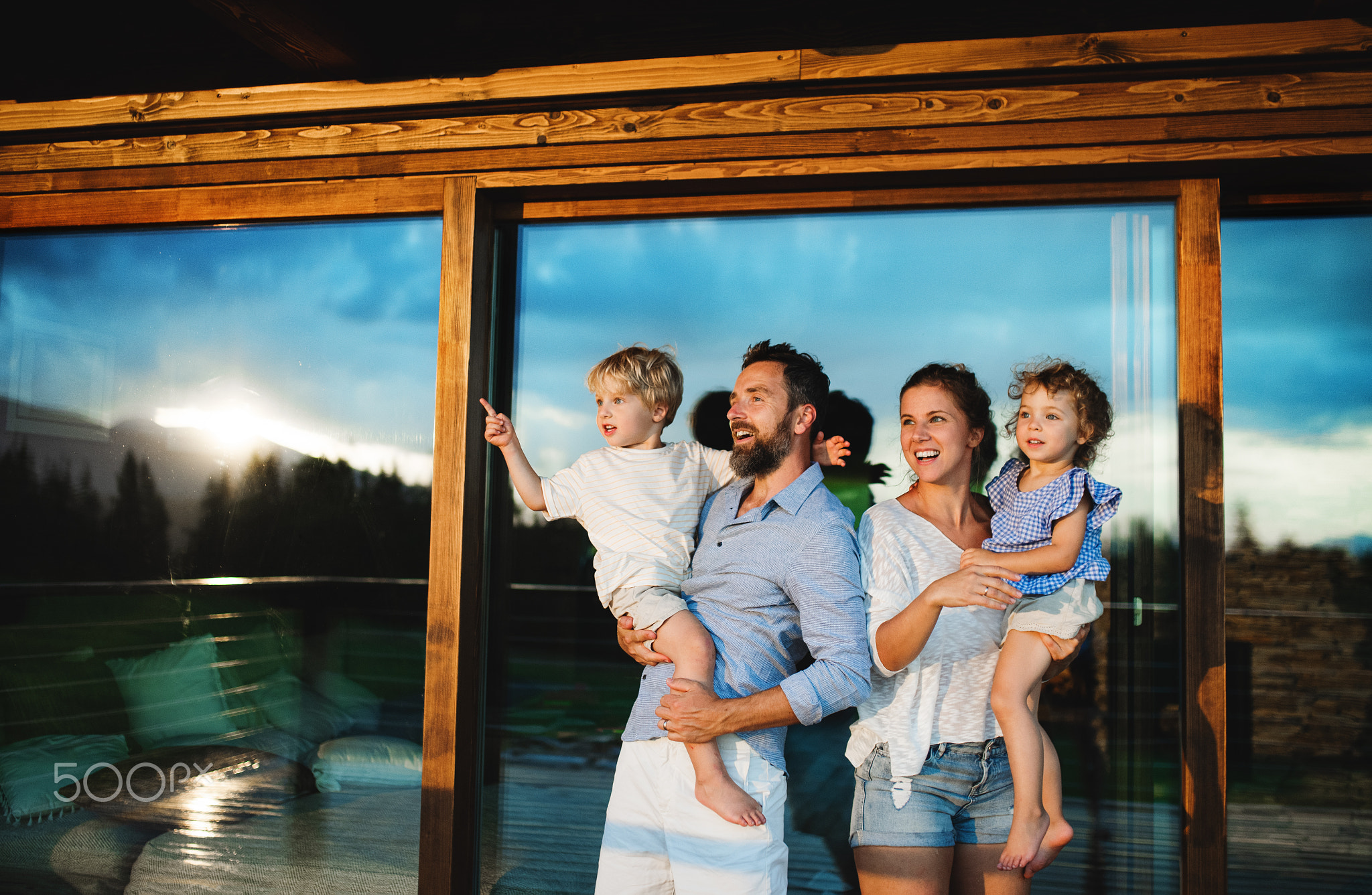Family with small children standing by wooden cabin, holiday in nature