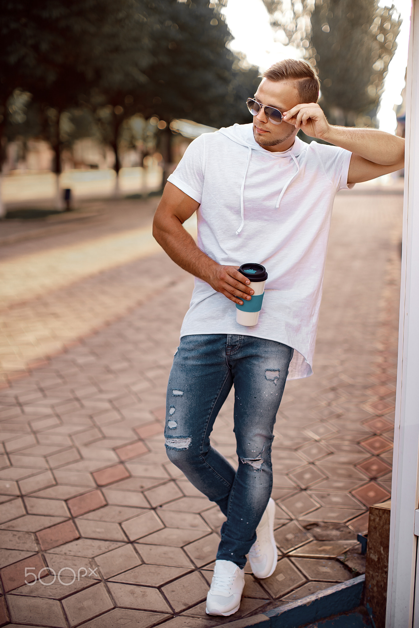 Young handsome man near city mall with cup of coffee and smartphone