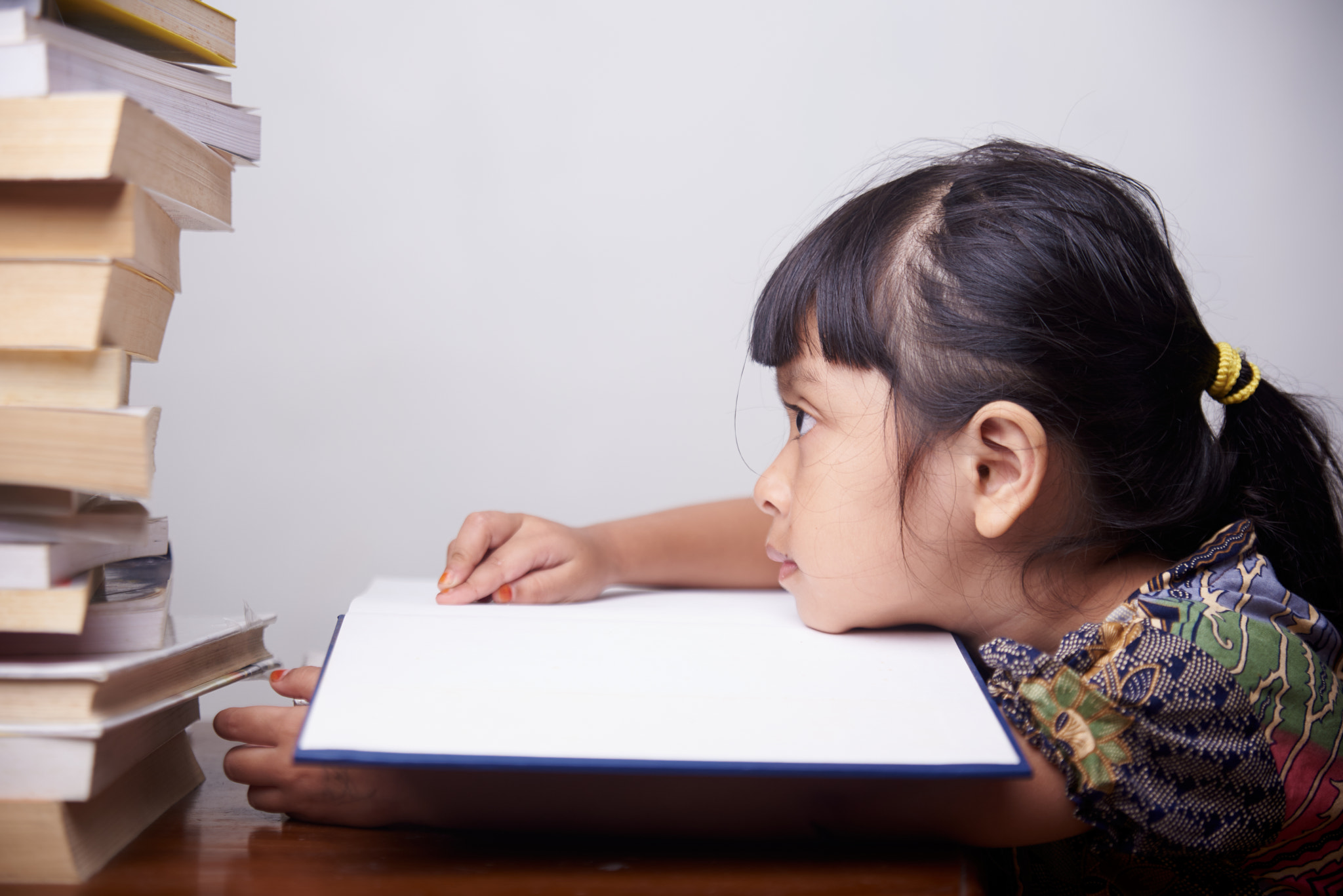 Bored little girl with a stack of books at home