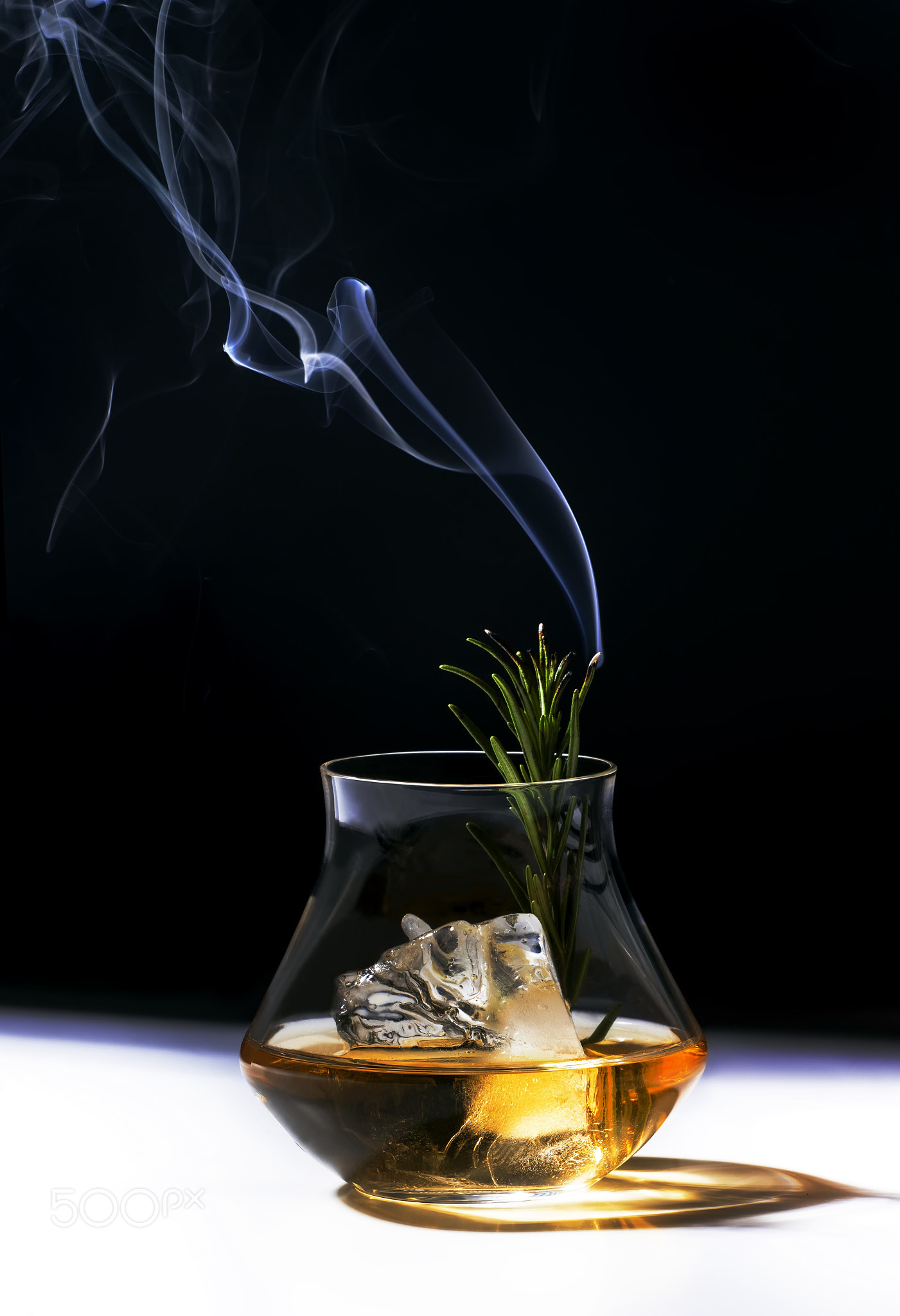 Contemporary still life with whiskey steaming rosemary, shard ice