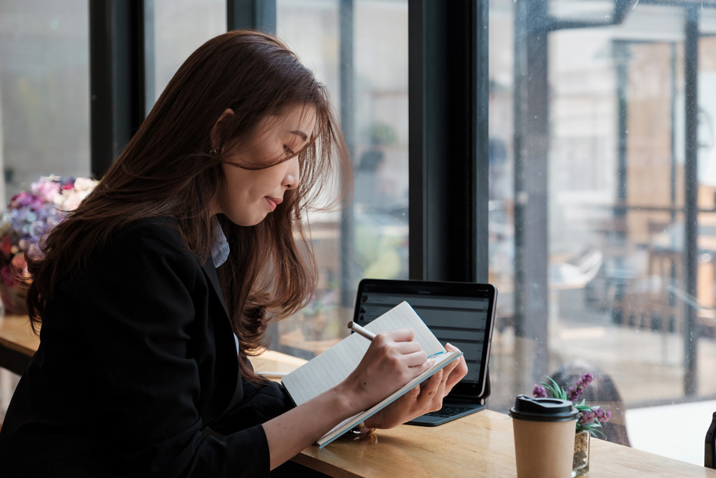 Une jeune femme écrit des informations à partir d'un ordinateur portable tout en se préparant par Worawee Meepian sur 500px.com